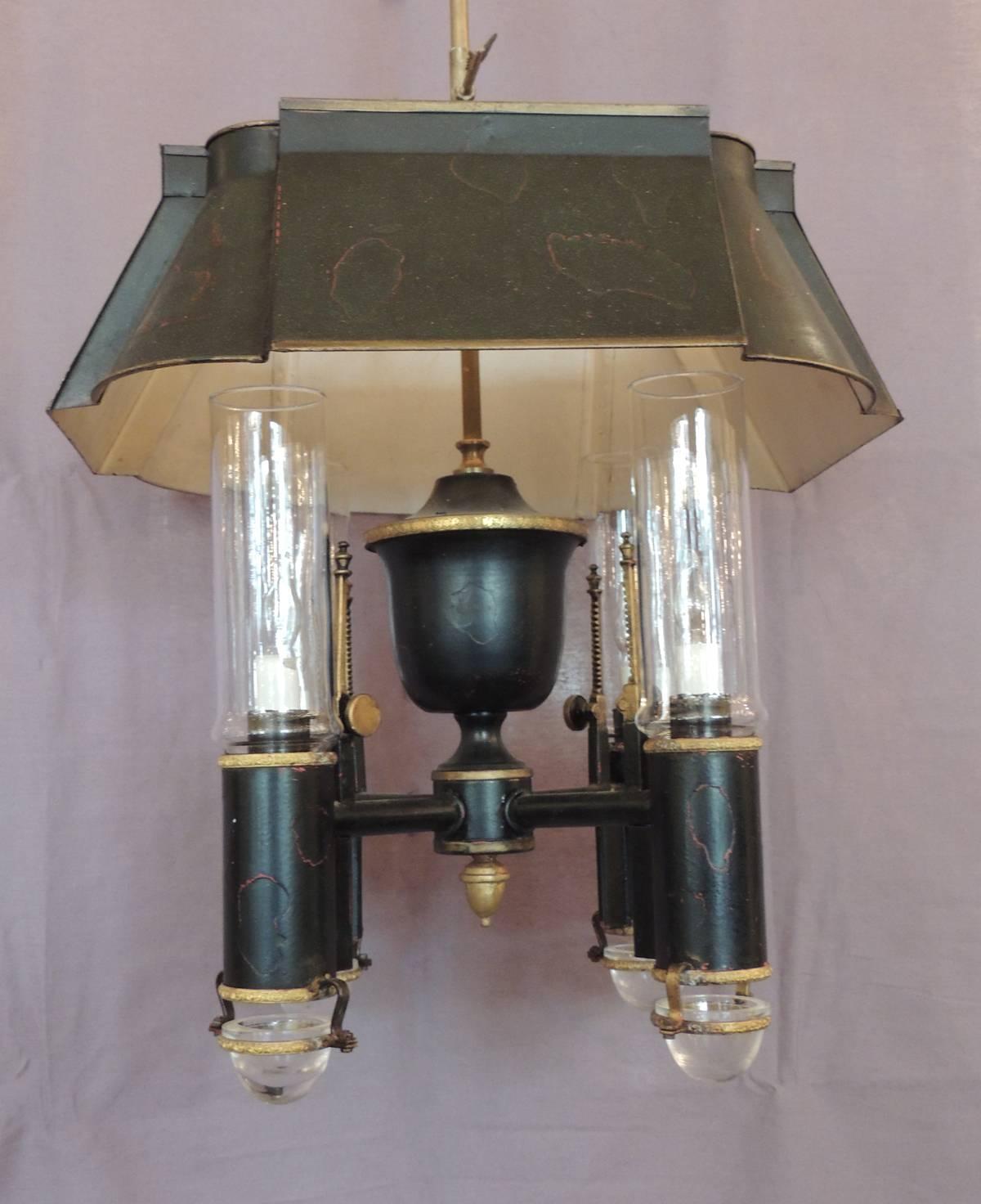 This chandelier was made in France in the 19th century, circa 1800, and features a tole shade surmounted over four lights. Each of the lights have a hurricane shade that fits perfectly into the argon shade. All the hardware is original and has been