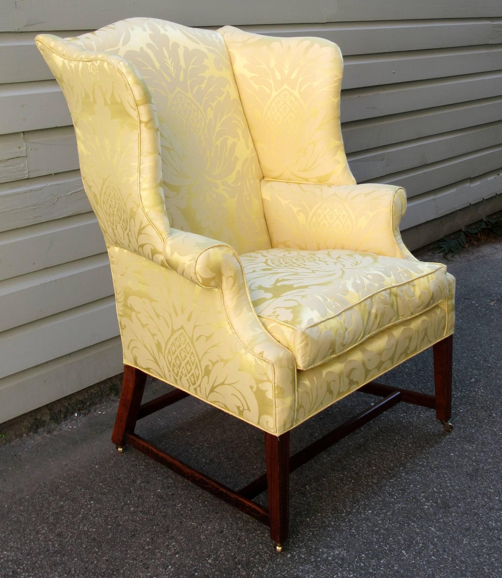 A federal upholstered wingback chair from Virginia, circa 1790, featuring new upholstery, a walnut frame with bell flower inlay on legs and new casters. The feet were reduced to accommodate the addition of the casters.
