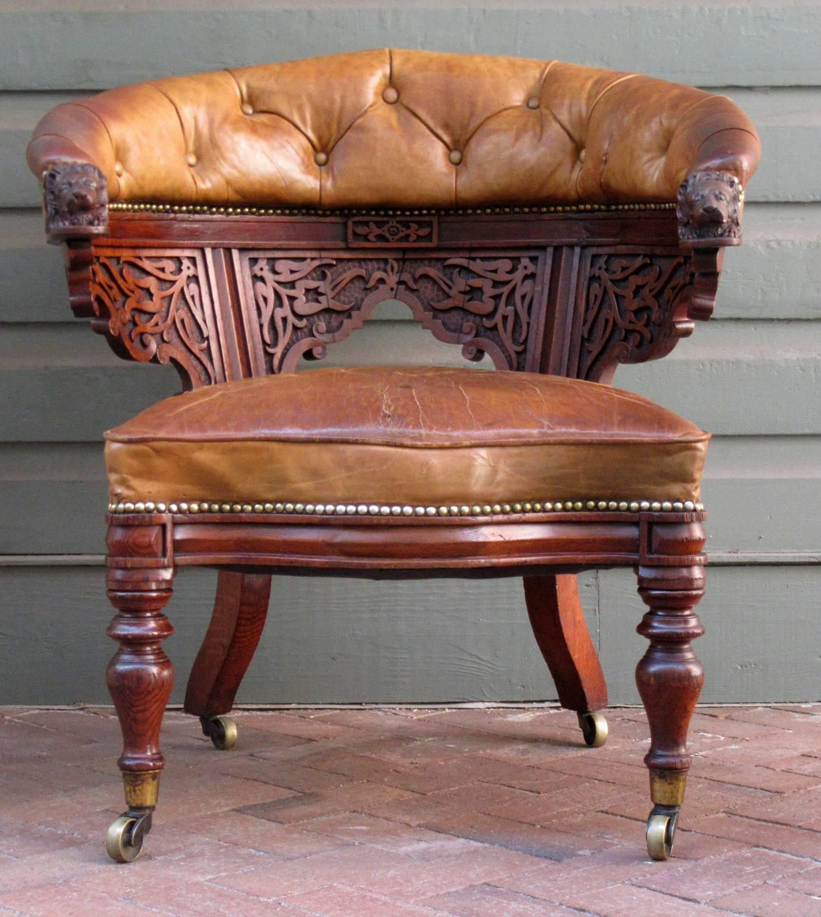 A handsome English oak barrel back gentleman's chair, circa 1820, featuring dramatic carvings with lion heads, original tufted leather upholstery and casters. The leather seat can has a clean tear approximately 8
