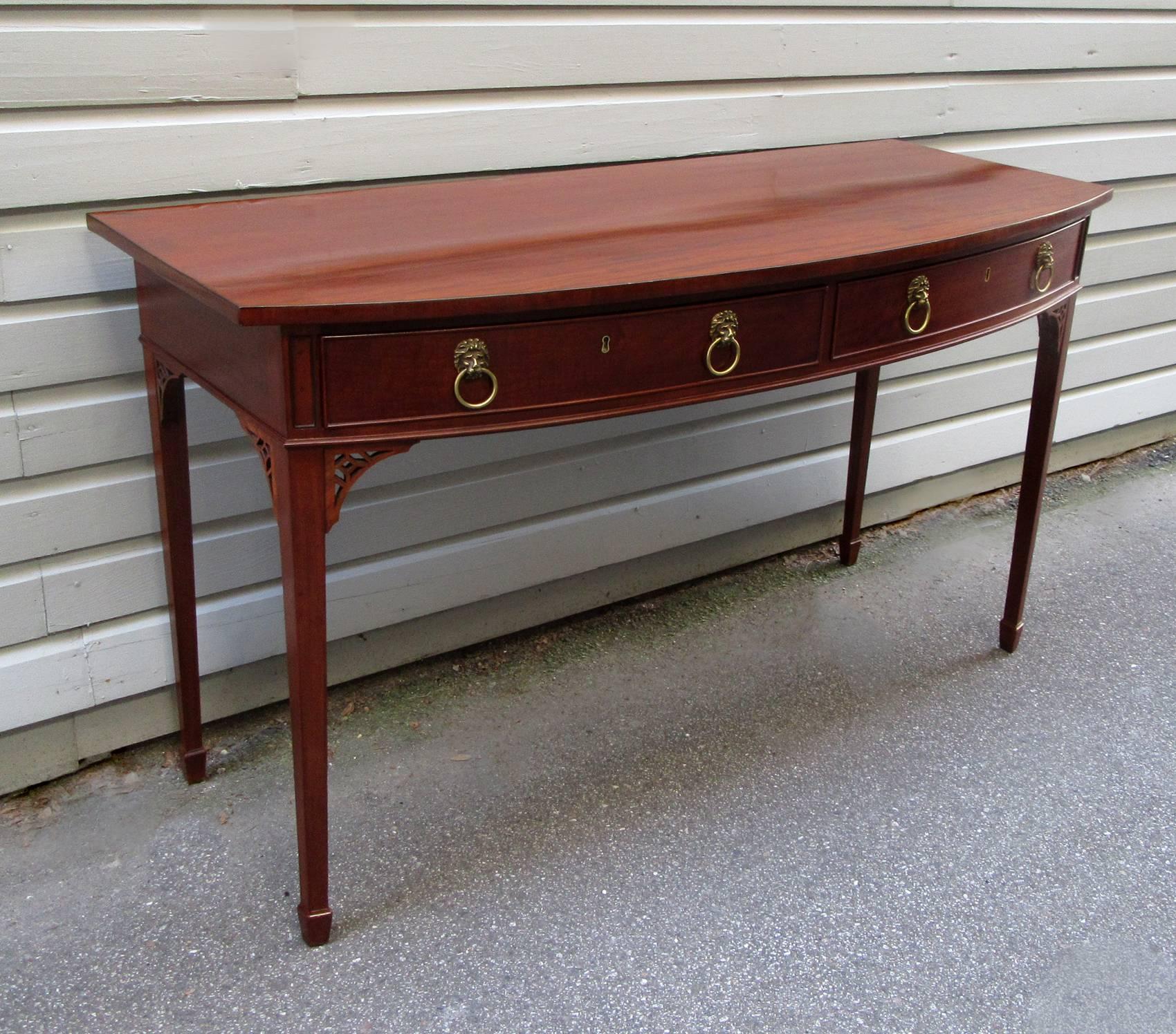 An English Georgian mahogany bow front table, circa 1815, featuring two drawers, fretwork and lion head brass pulls. Stamped by noted English furniture maker Williamson & Sons, Guildford.