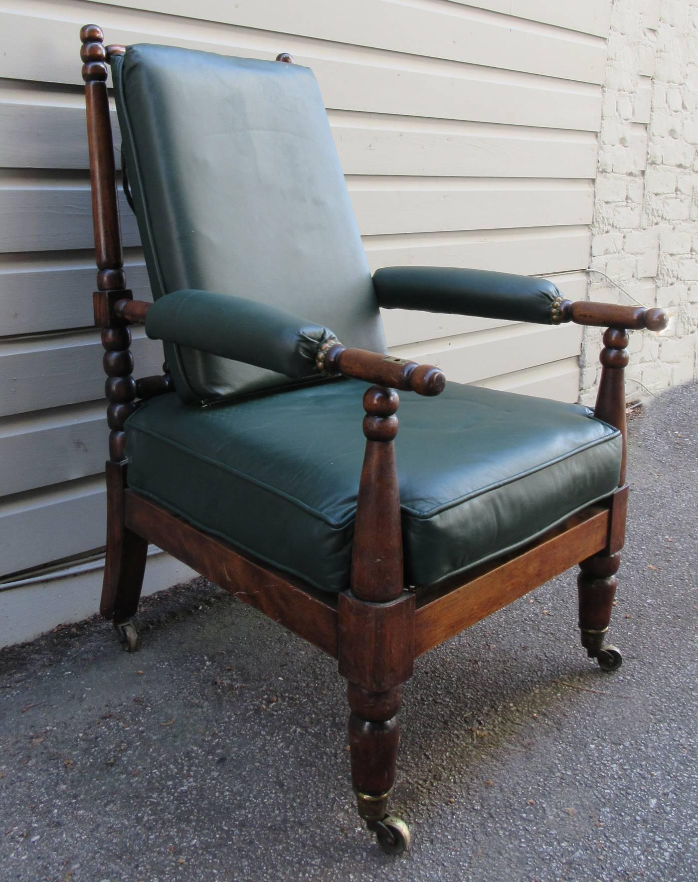 An English mahogany library chair, circa 1830, featuring bobbin turned frame, dark green leather upholstery and original casters.