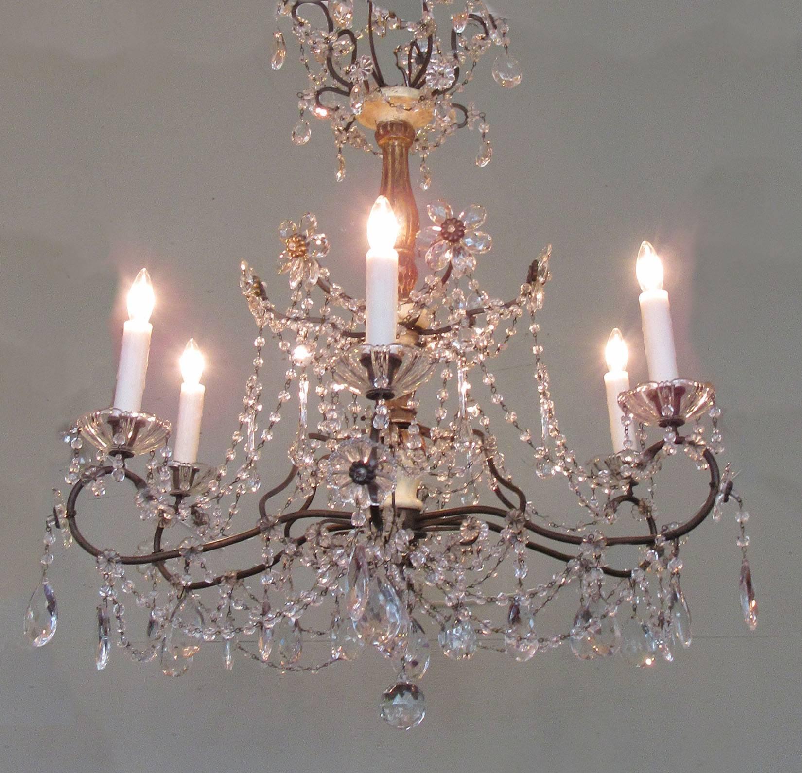 An Italian Genoese crystal chandelier, circa 1920, featuring a giltwood and ivory painted stem and six candle bulb tole arms adorned with crystal beaded swag, pendants and rosettes.