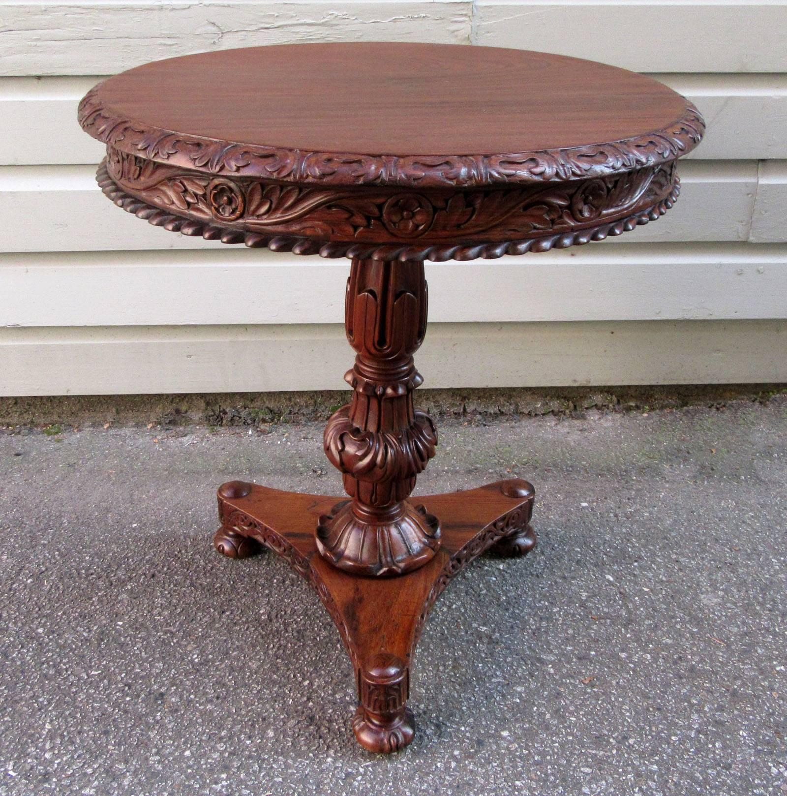 A British Colonial Regency solid rosewood table made in India, circa 1830, featuring an elaborately carved apron and tripod pedestal base with bun feet.