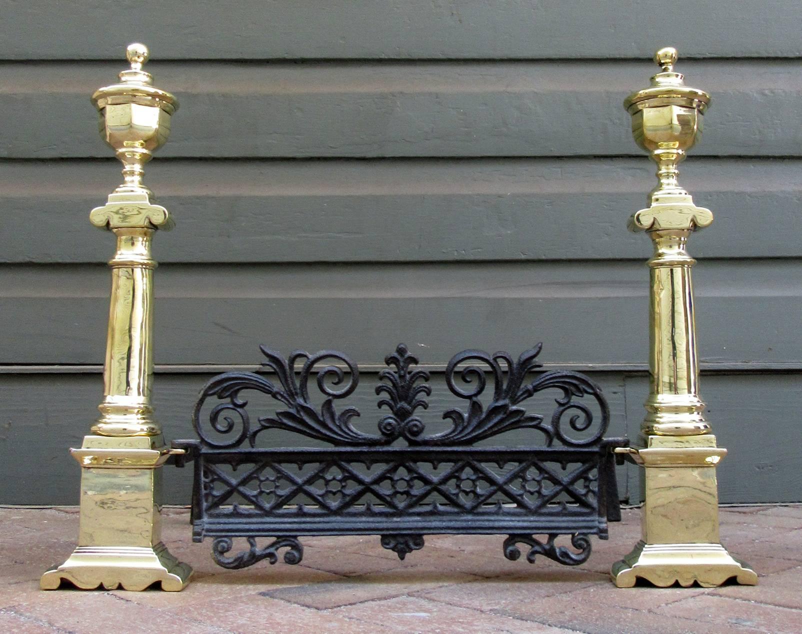 A rare pair of Charleston neoclassical brass andirons, circa 1810, with the original cast iron fender. The total width of the andirons and fender set is 24.75