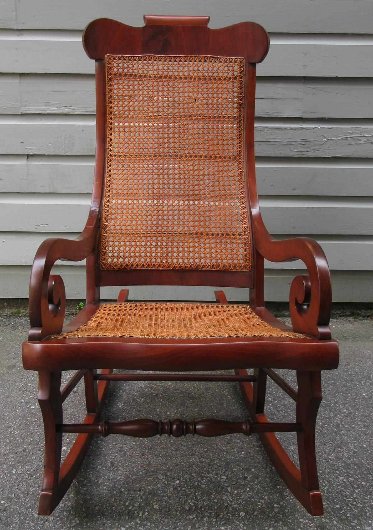 A Caribbean mahogany and cane rocking chair from St. Croix, circa 1830, featuring Regency scroll arms, clean lines and handwoven caning.