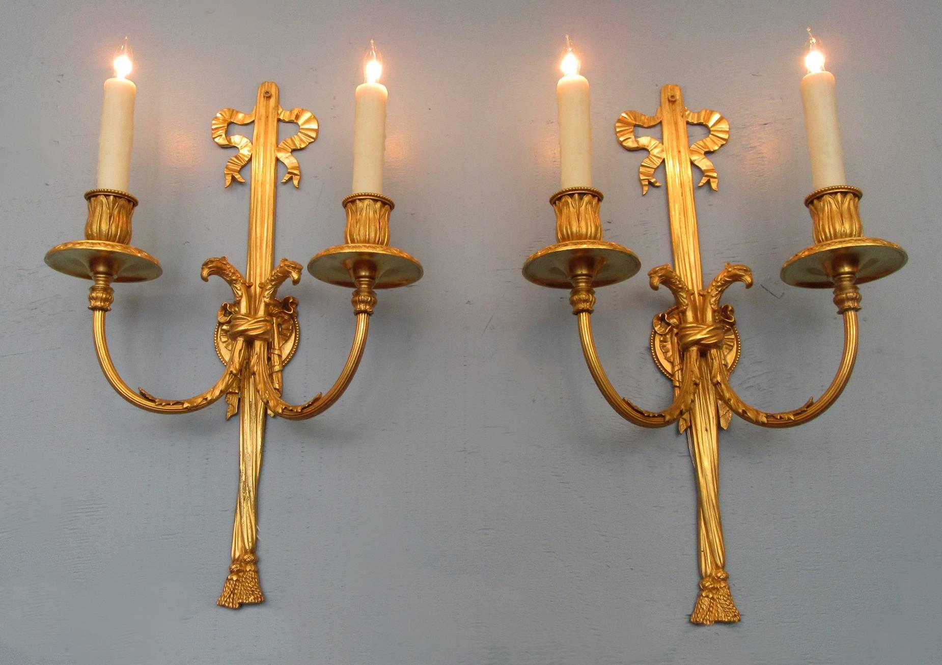 An elegant pair of bronze doré Regence style sconces from New York, circa 1910 and stamped by noted maker Edward F. Caldwell & Co., each featuring two candle arms with ribbon, opposing Ho Ho birds and tassel. The sconces have recently been rewired