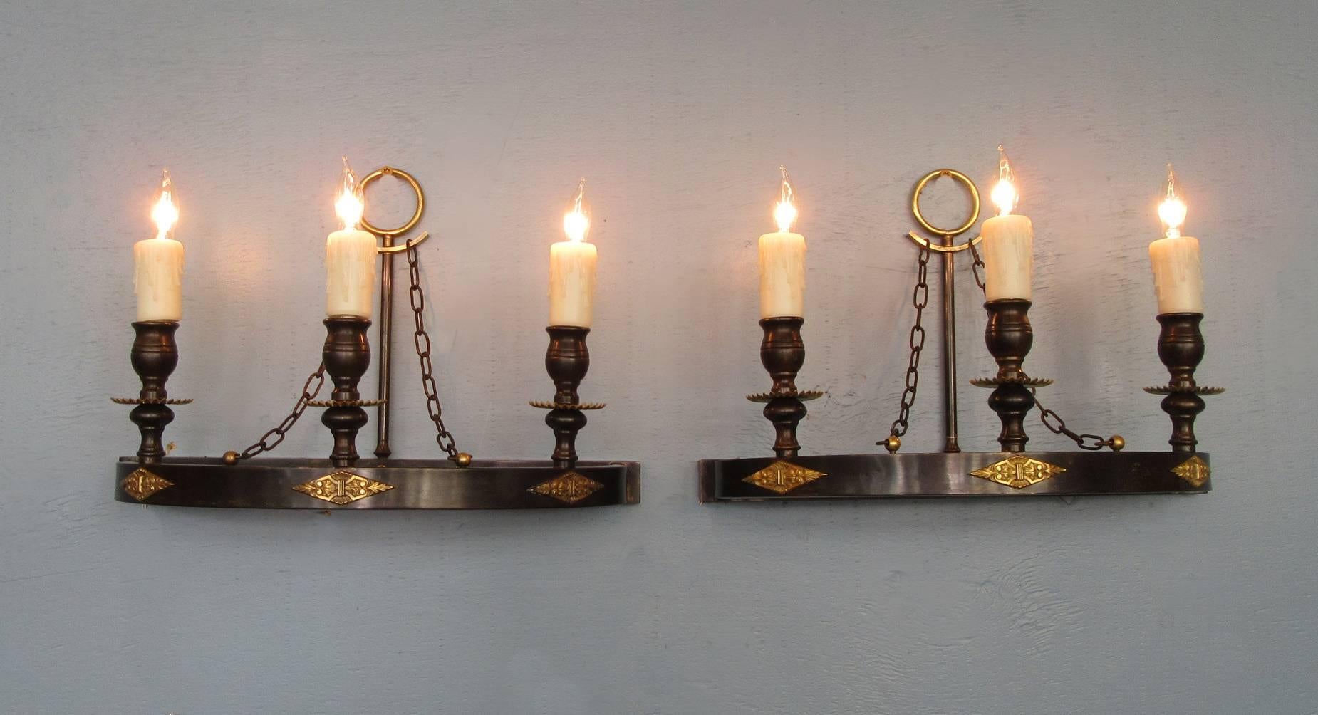An early 20th century pair of Italian Empire sconces, circa 1920, with patinated bronze demilune shape bases featuring three candle bulbs and brass applique. The sconces have been rewired with new porcelain sockets.