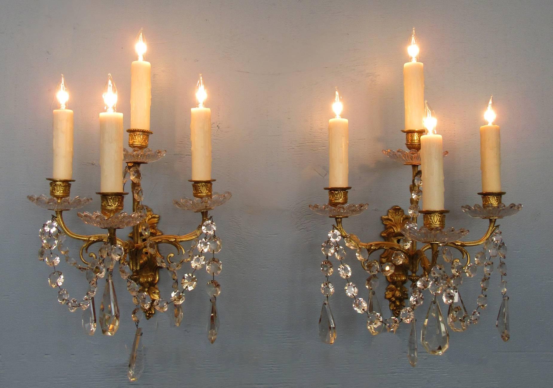 An elegant pair of 19th century French Regence sconces, circa 1820, each featuring four candle arms, Baccarat quality crystals and bobeche. The pair were originally candle but have been recently cleaned and rewired with new porcelain sockets.