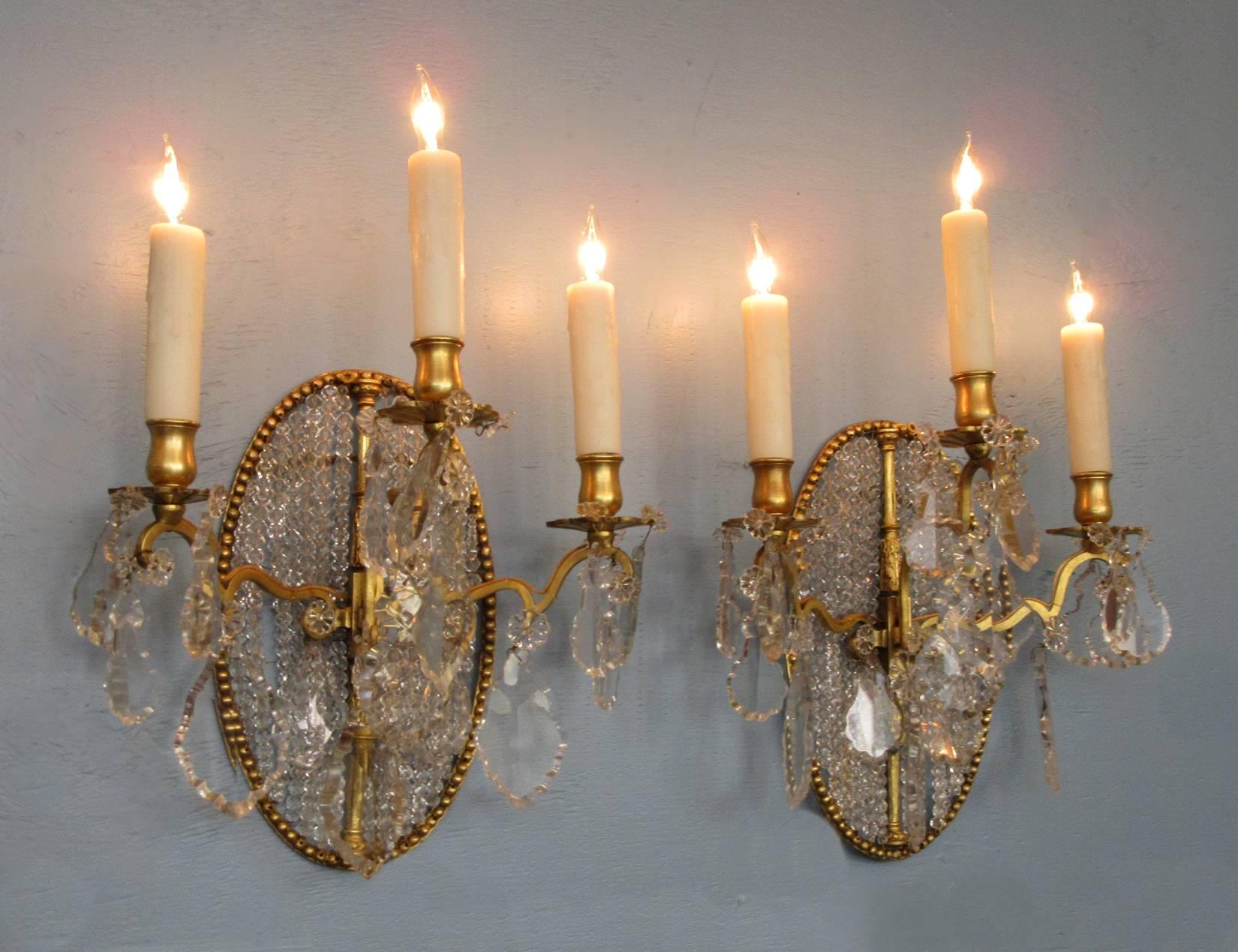 A pair of 19th century Italian neoclassical bronze doré and crystal sconces, circa 1830, each featuring three candle arms and beaded crystal medallion back. The pair have recently been cleaned and rewired with porcelain sockets.
 