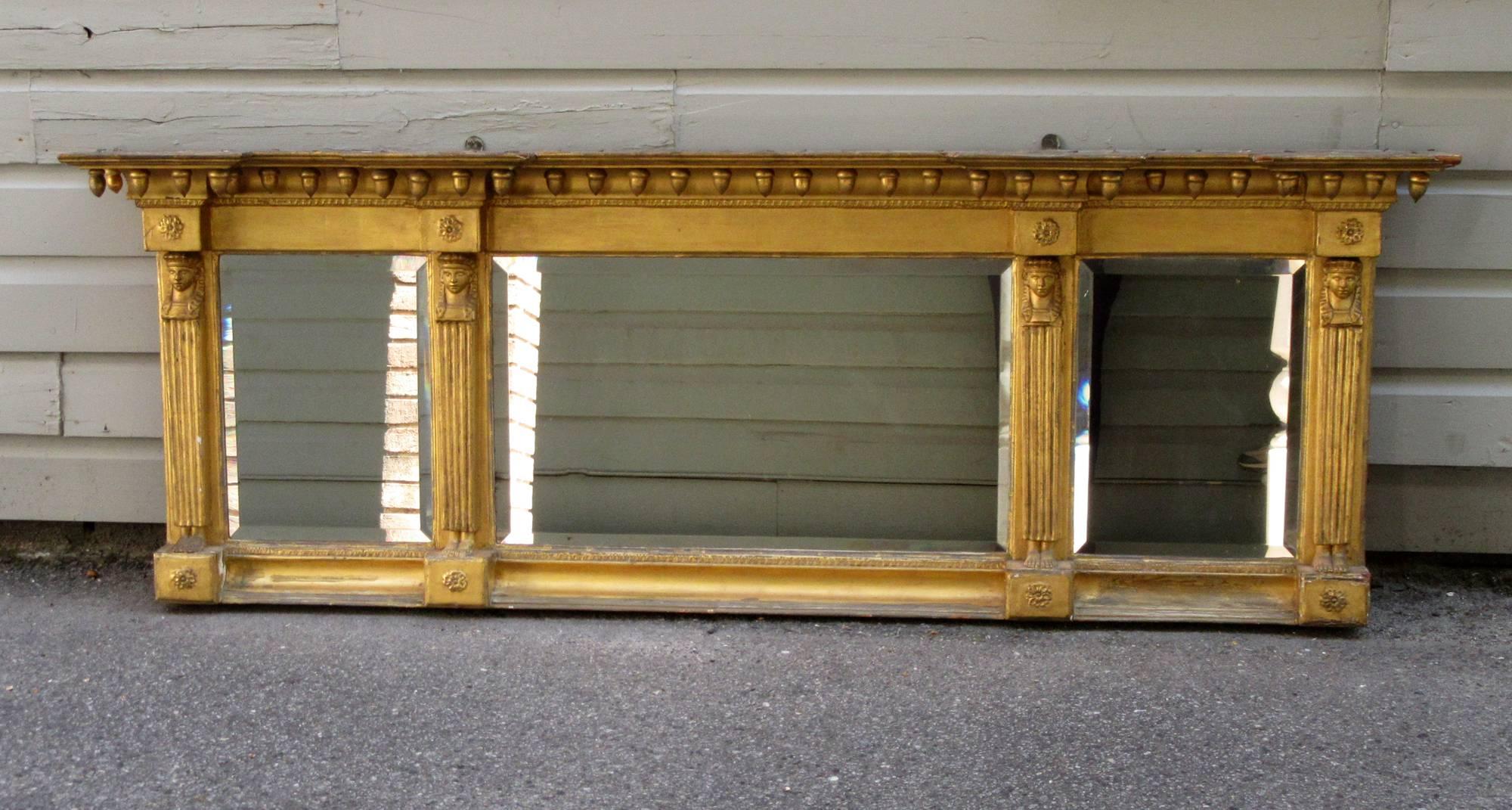 An early 19th century English (possibly American) Egyptian Revival giltwood and gesso overmantel mirror, circa 1820, featuring original beveled glass and pharaoh motifs accented with acorns. The mirror glass was recently re-silvered.