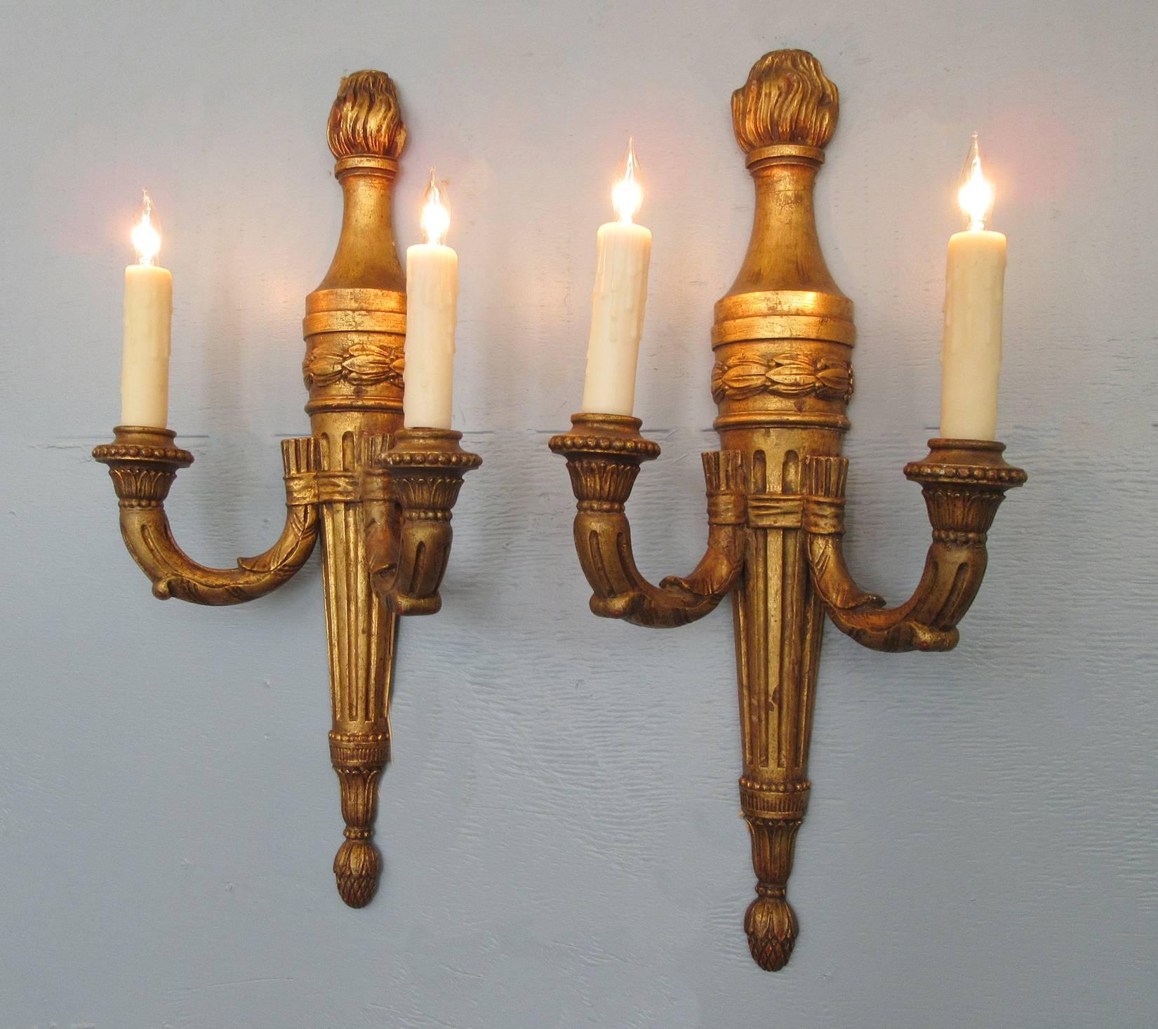 A pair of early 20th century Italian giltwood sconces, circa 1920, each featuring two candle arms fastened to hand-carved fluted torch frames. The pair have been recently been cleaned and rewired with new porcelain sockets.