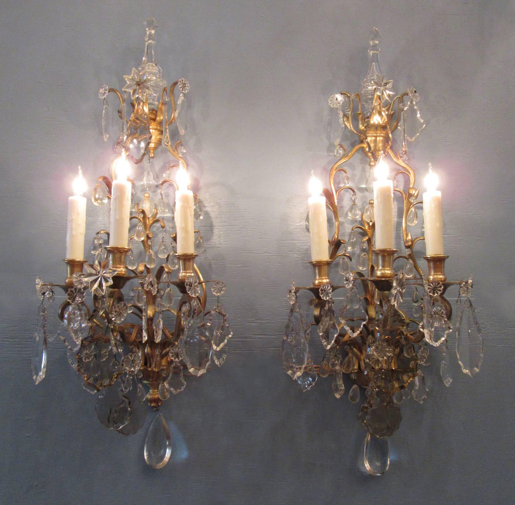 A large pair of 19th century French Louis XIV bronze doré and crystal sconces, circa 1830, each featuring three candle arms and large clear and smokey cut and polished crystal pendants. The pair have recently been cleaned and rewired with new
