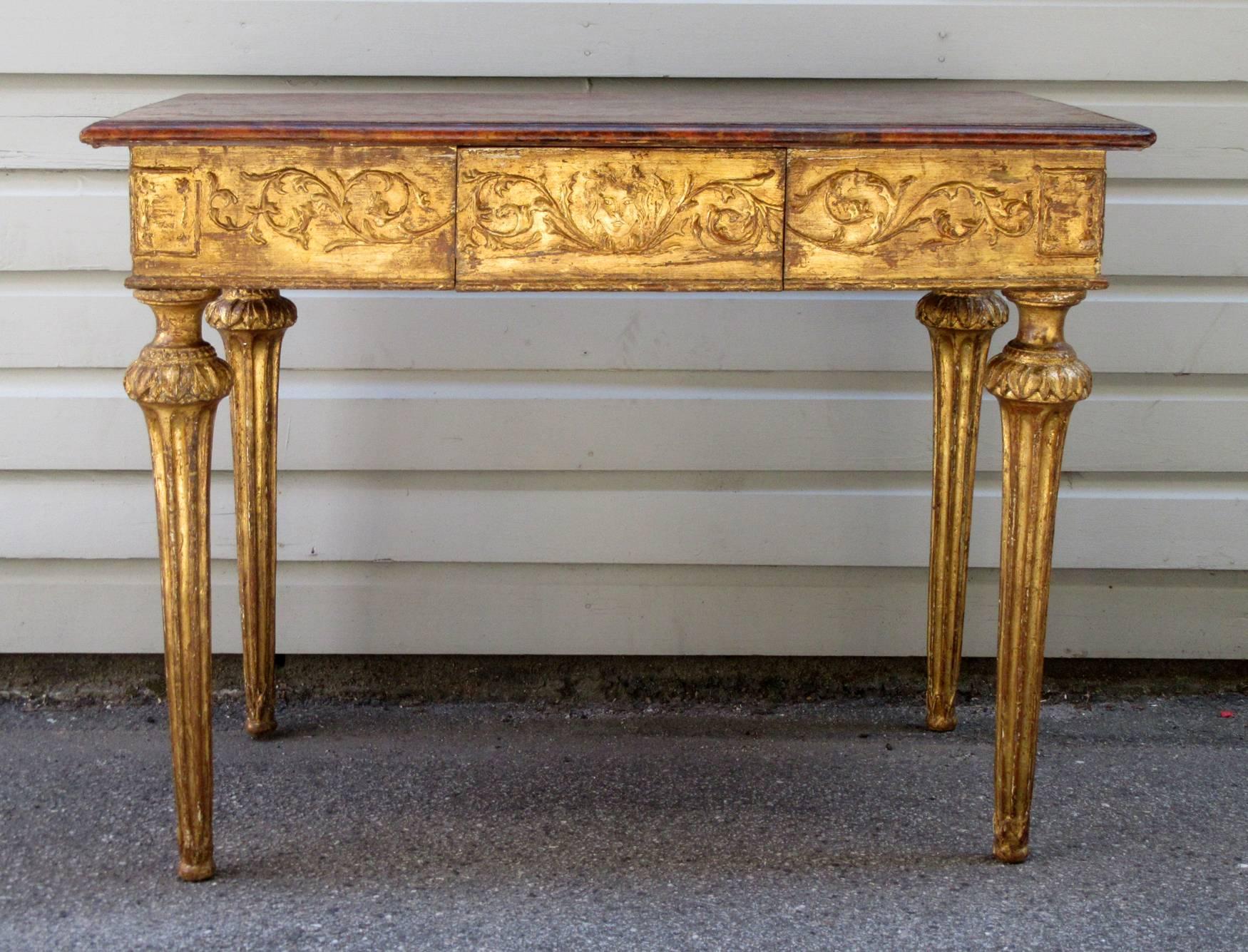 An 18th century Italian Baroque giltwood pine table, circa 1760, finished all the way around with exceptional details and featuring faux marbleized top, fluted trumpet legs and one drawer.