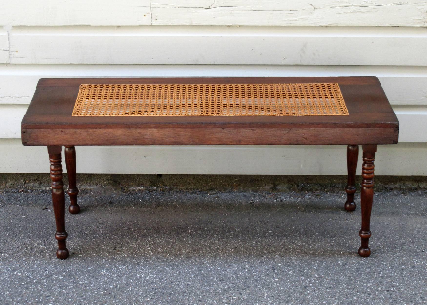 An early 19th century Caribbean Campaign mahogany and hand-caned bench from Jamaica, circa 1820, featuring finely turned legs and iron stretchers. The legs collapse and fold down into the frame. The caning is new but was hand-done recently by a