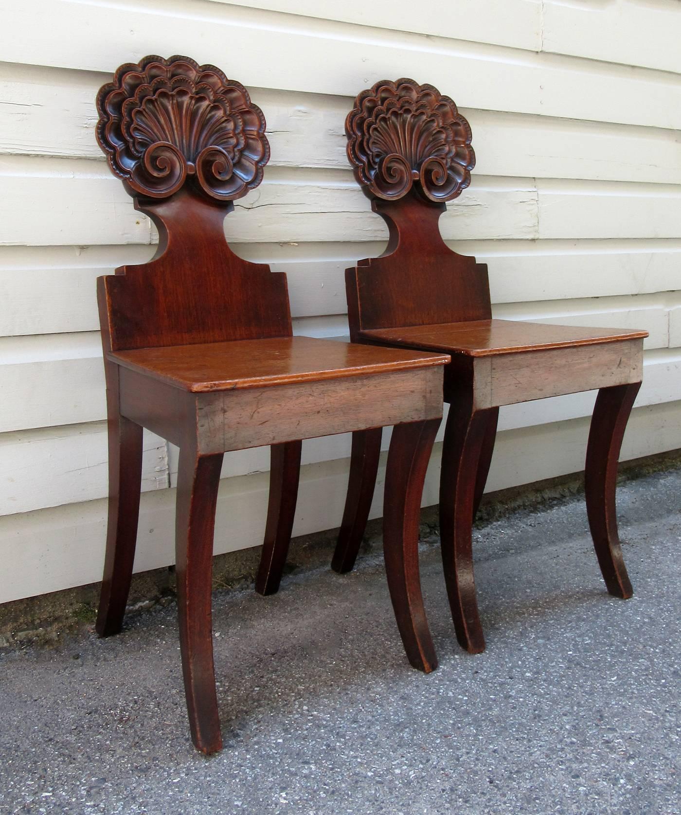 A pair of 19th century English William IV mahogany hall chairs, circa 1830, attributed to noted furniture maker Gillows of London and featuring an intricately carved stylized shell back with sabre legs.
 