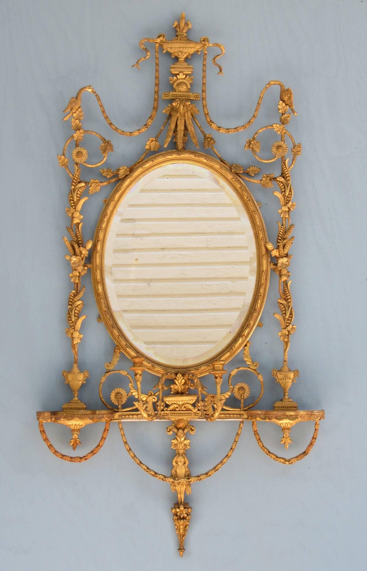 A stunning pair of 19th century English Adams giltwood mirrors, circa 1800, each featuring original beveled mirror plate, two girandole candle arms and two shelf brackets. The giltwood motifs on each mirror feature Ho Ho birds, sheaths of wheat,
