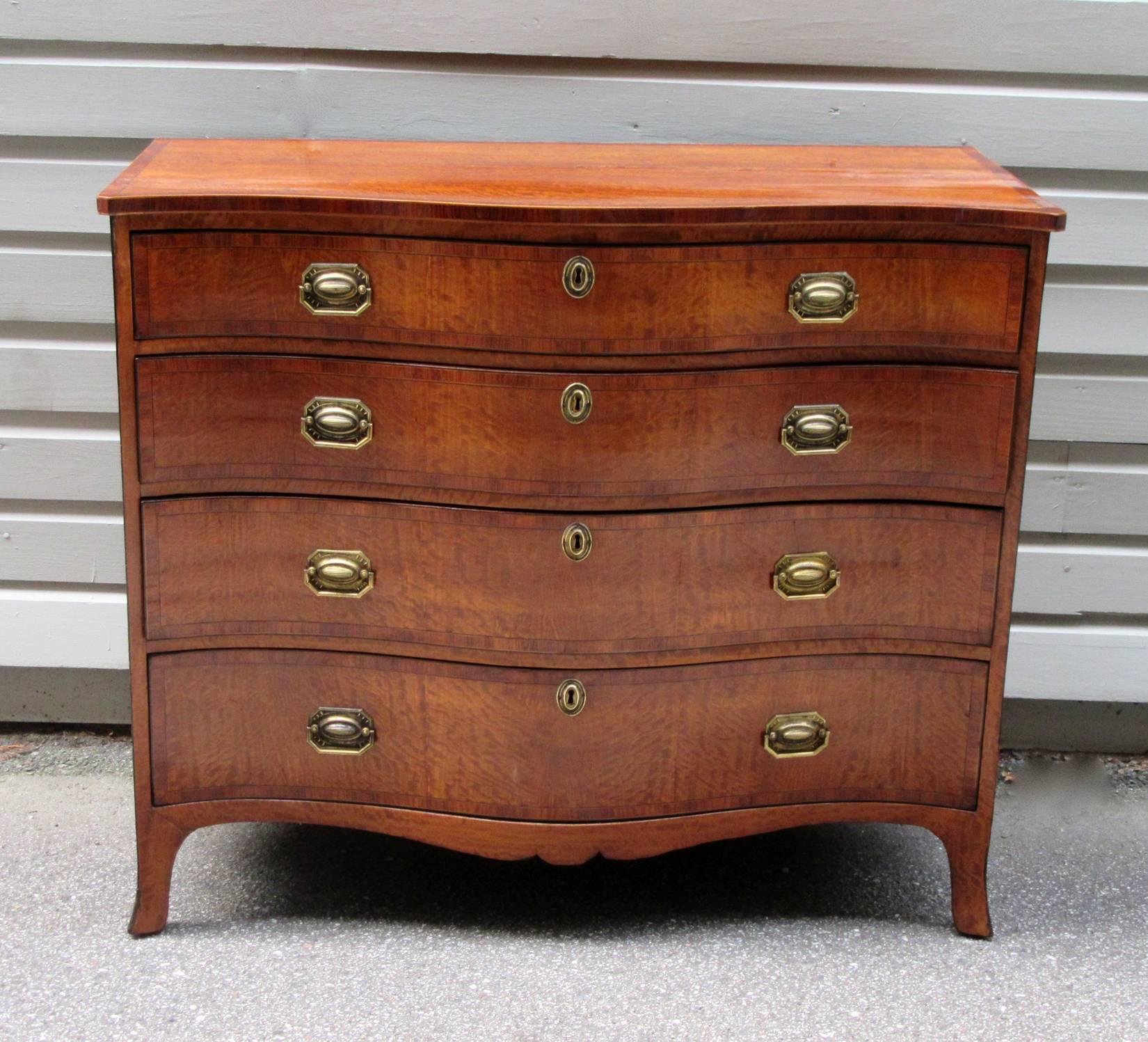 A period English Georgian satinwood serpentine chest of drawers, circa 1780, featuring four drawers, a top drawer with three dividers, French feet and original brass pulls. The chest is in excellent condition.