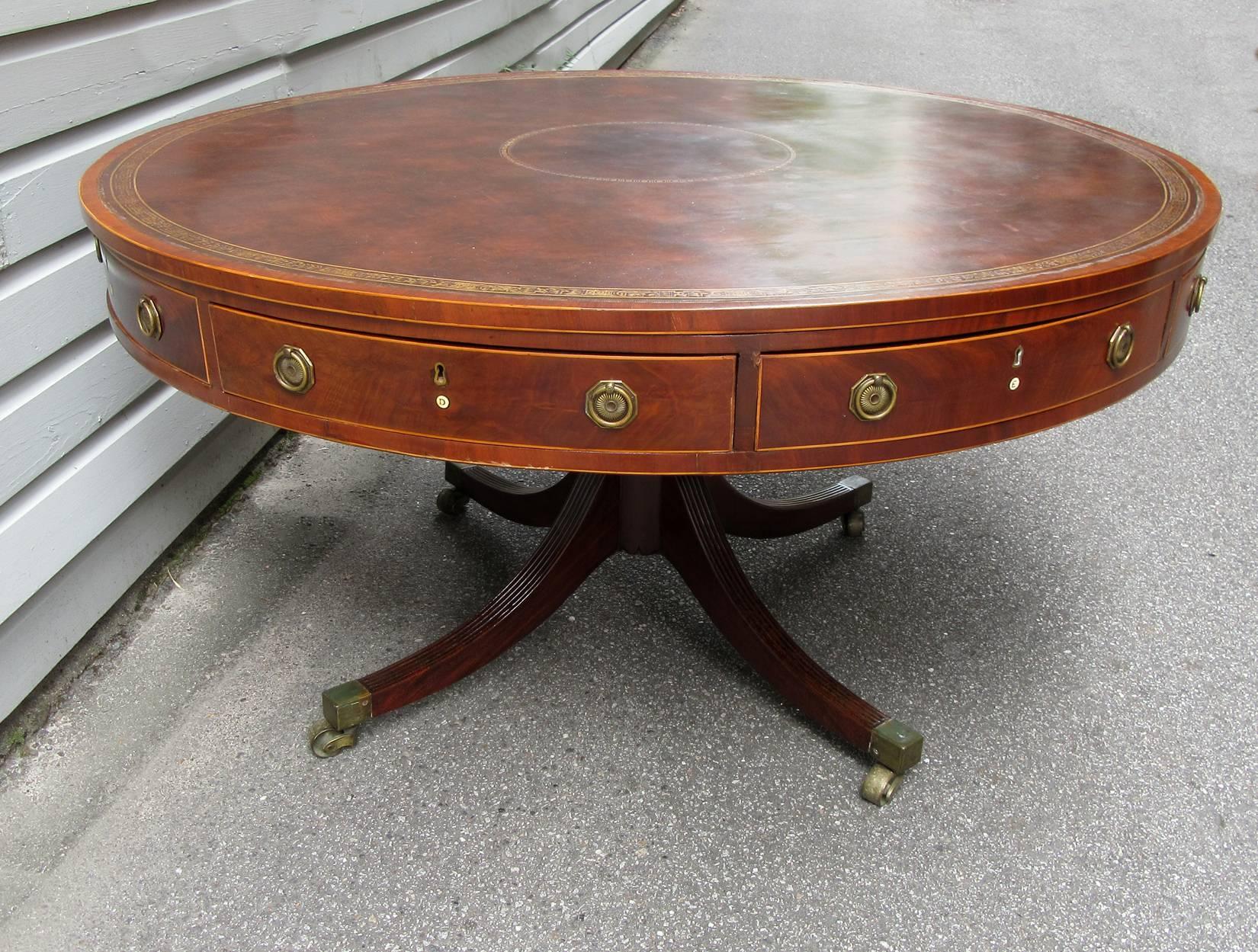 A large scale early 19th century English Regency mahogany rent table, circa 1810, with Egyptian motif embossed leather top, original brass hardware and eight drawers each labeled A, B, C, D, F, G, H.  The drum table sits on a  pedestal base with