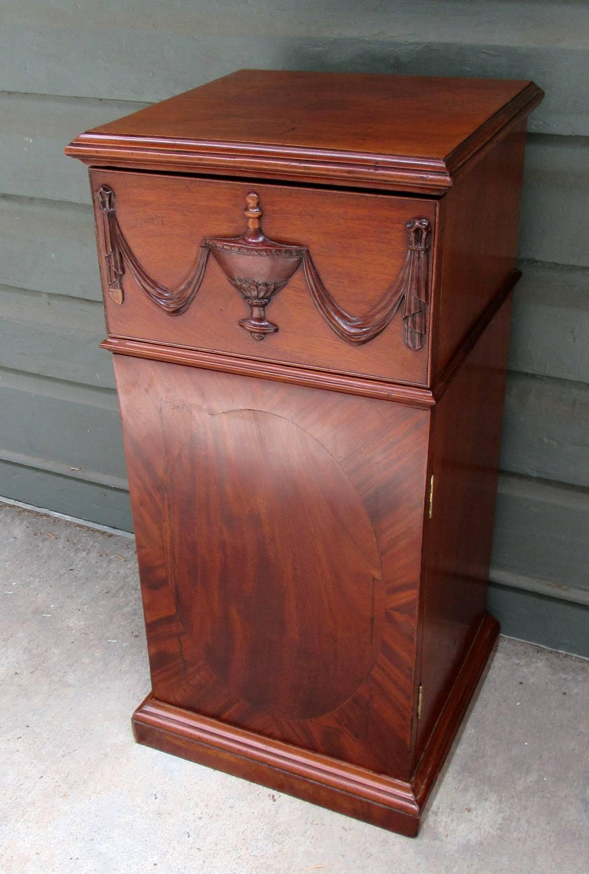 An early 19th century English Regency mahogany pedestal cabinet, circa 1810, featuring an urn with swag carved drawer and single cabinet door below.