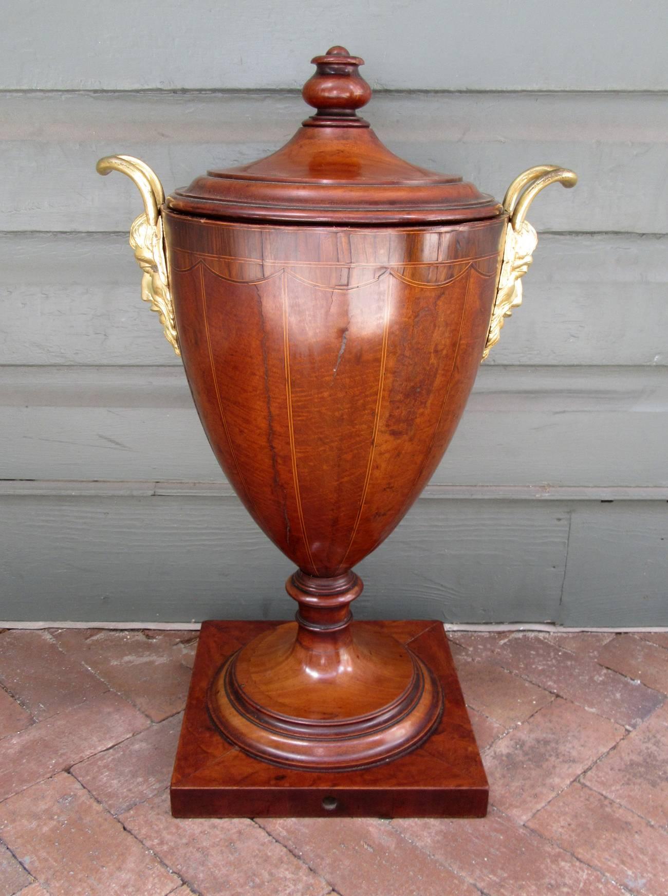 A late 18th century English George III mahogany urn or wine cooler on square base, circa 1780, featuring bronze doré mounted handles with Bacchus, double lids and original liner that has been coated with sealant. The base is 12