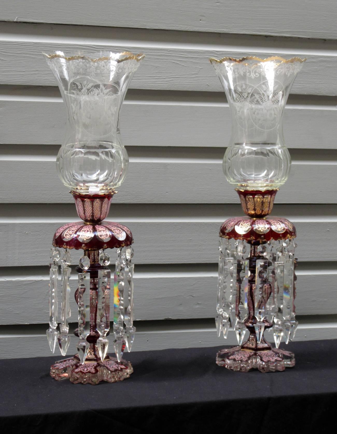 A sizable pair of late 19th century French Baccarat cranberry crystal lusters, circa 1880, accented with rose and gilt enameling and etched crystal hurricanes featuring floral bouquet motifs.