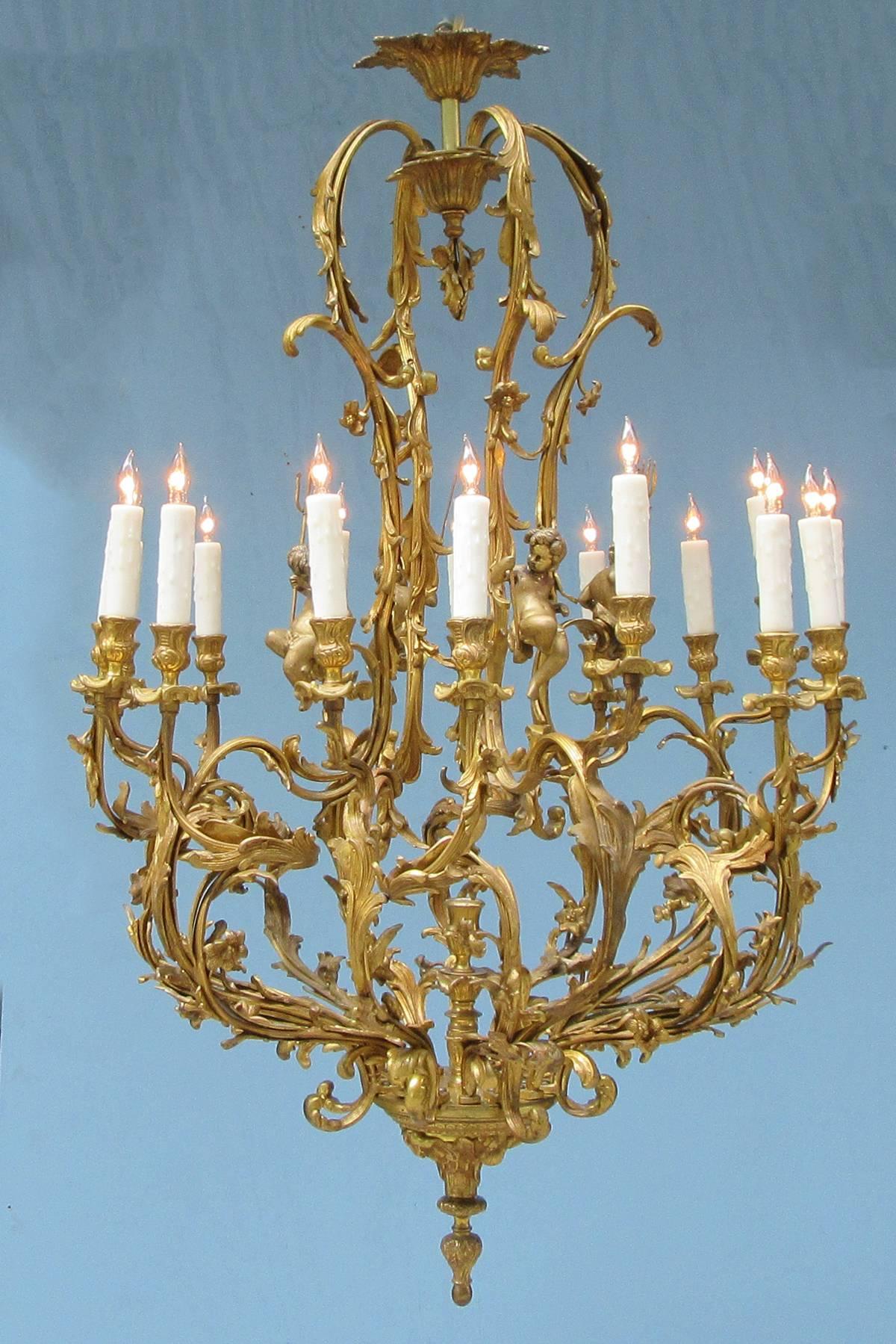 A large-scale early 20th century French Louis XIV style bronze doré chandelier, circa 1900, with sixteen candle arms and a centre candleholder. The chandelier has foliate casting accented with flowers and triton holding putti, the chandelier has