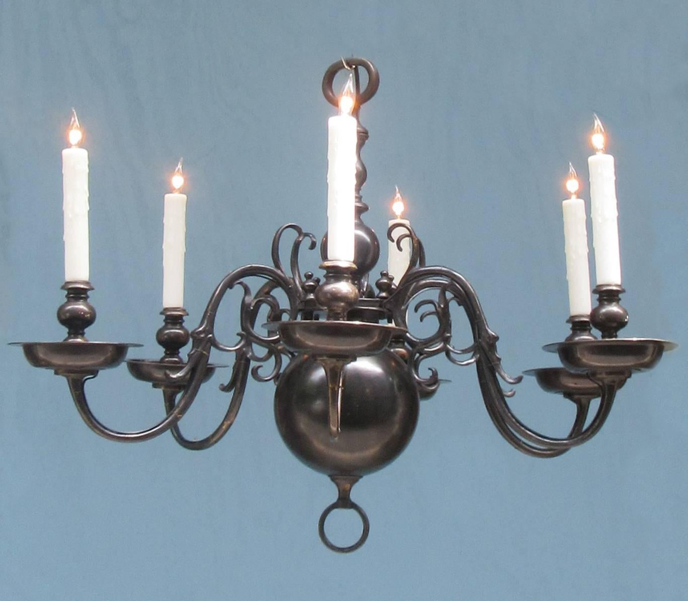 An early 20th century American chandelier in Dutch Colonial style, circa 1910, with eliptical shaped top ring and bulbous black patinated body featuring six candle arms adorned with foliate scrollwork. The chandelier has recently been rewired with