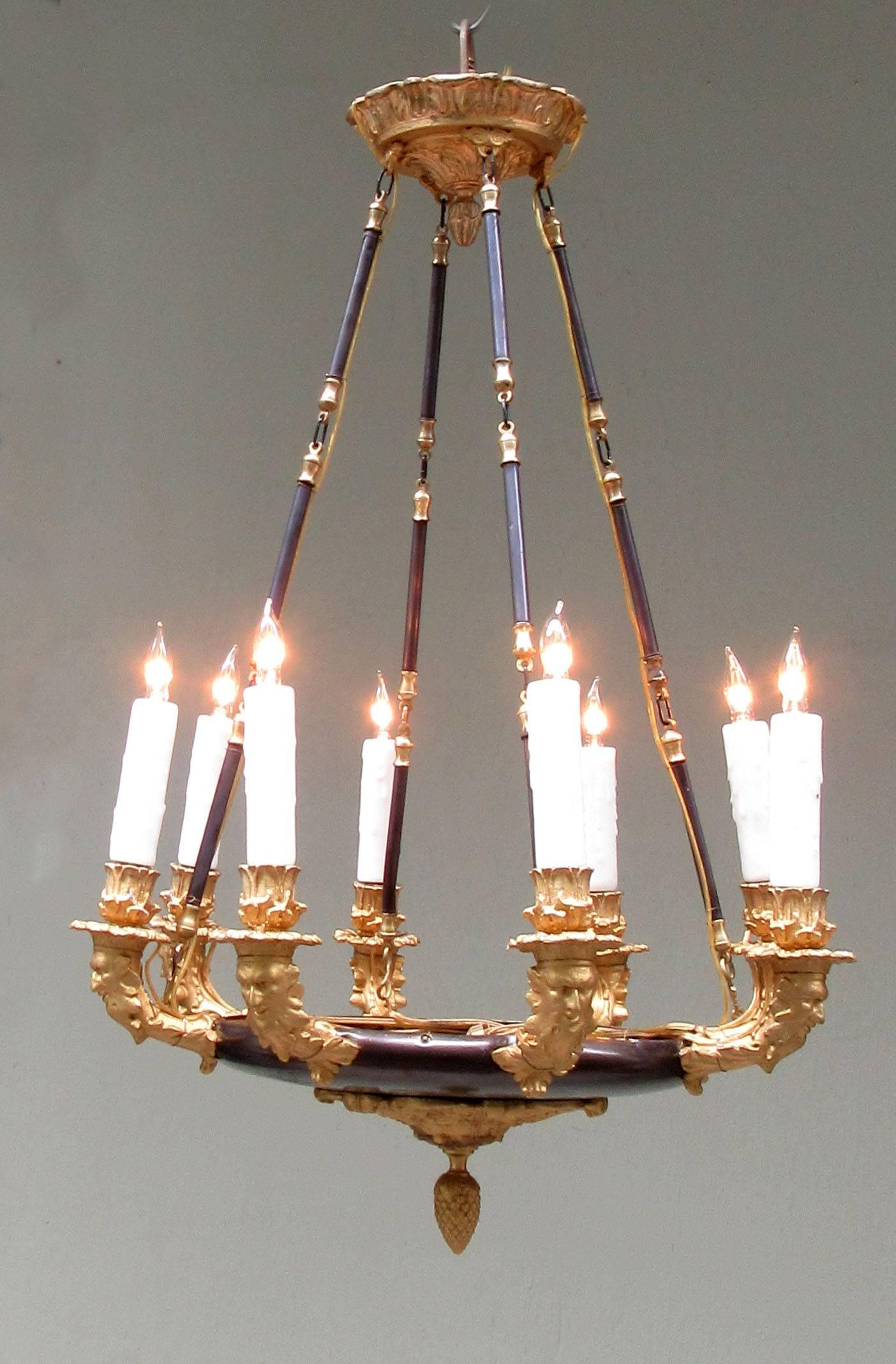 A 19th century French Empire chandelier, circa 1840, made of patinated brass and zinc and featuring eight candle arms adorned with north winds faces and pine cone finial. The chandelier has recently been cleaned, rewired and has new porcelain