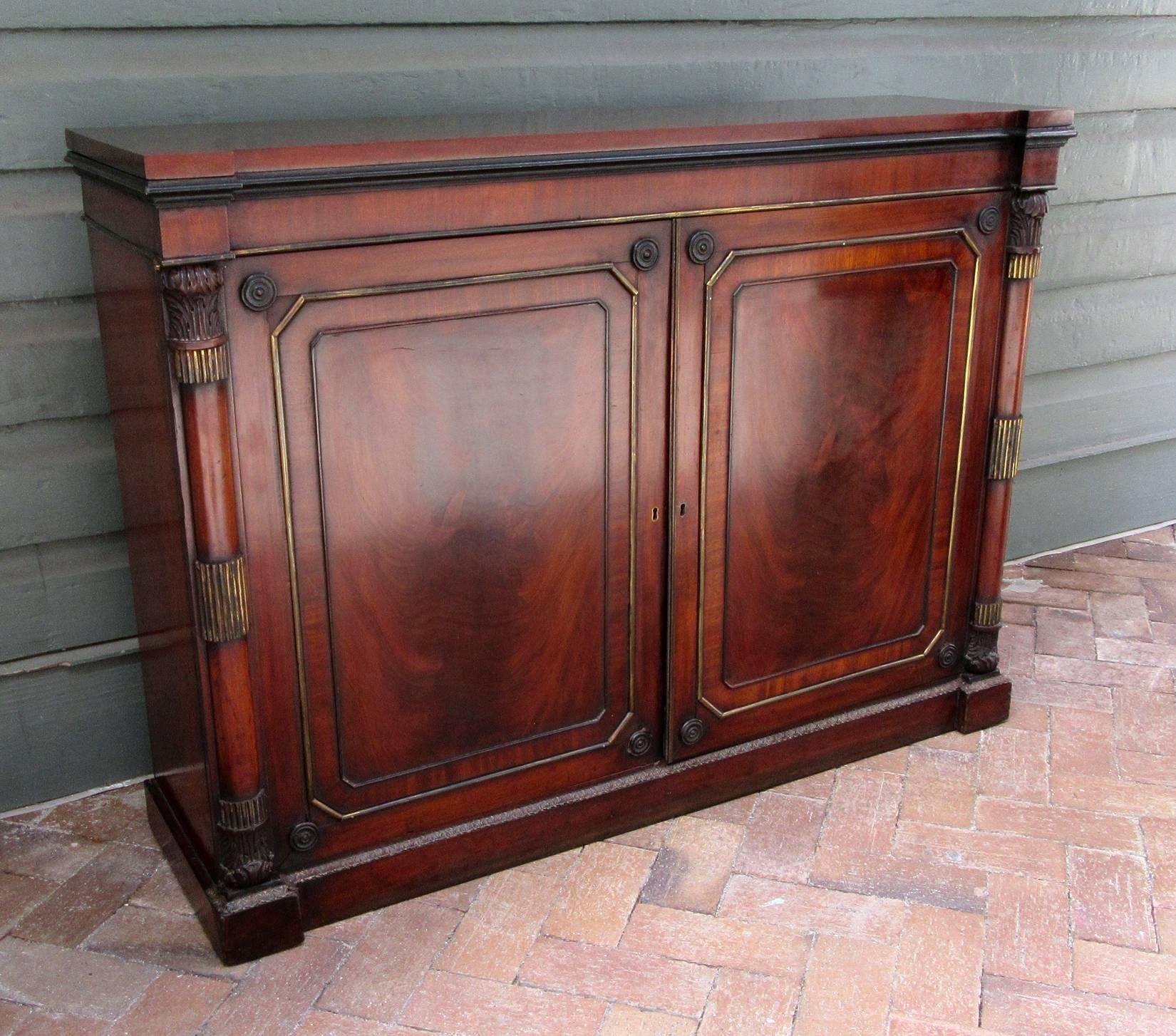 An early 19th century English Regency mahogany two-door cabinet or credenza, circa 1810, with neoclassical columns, brass fittings and key.