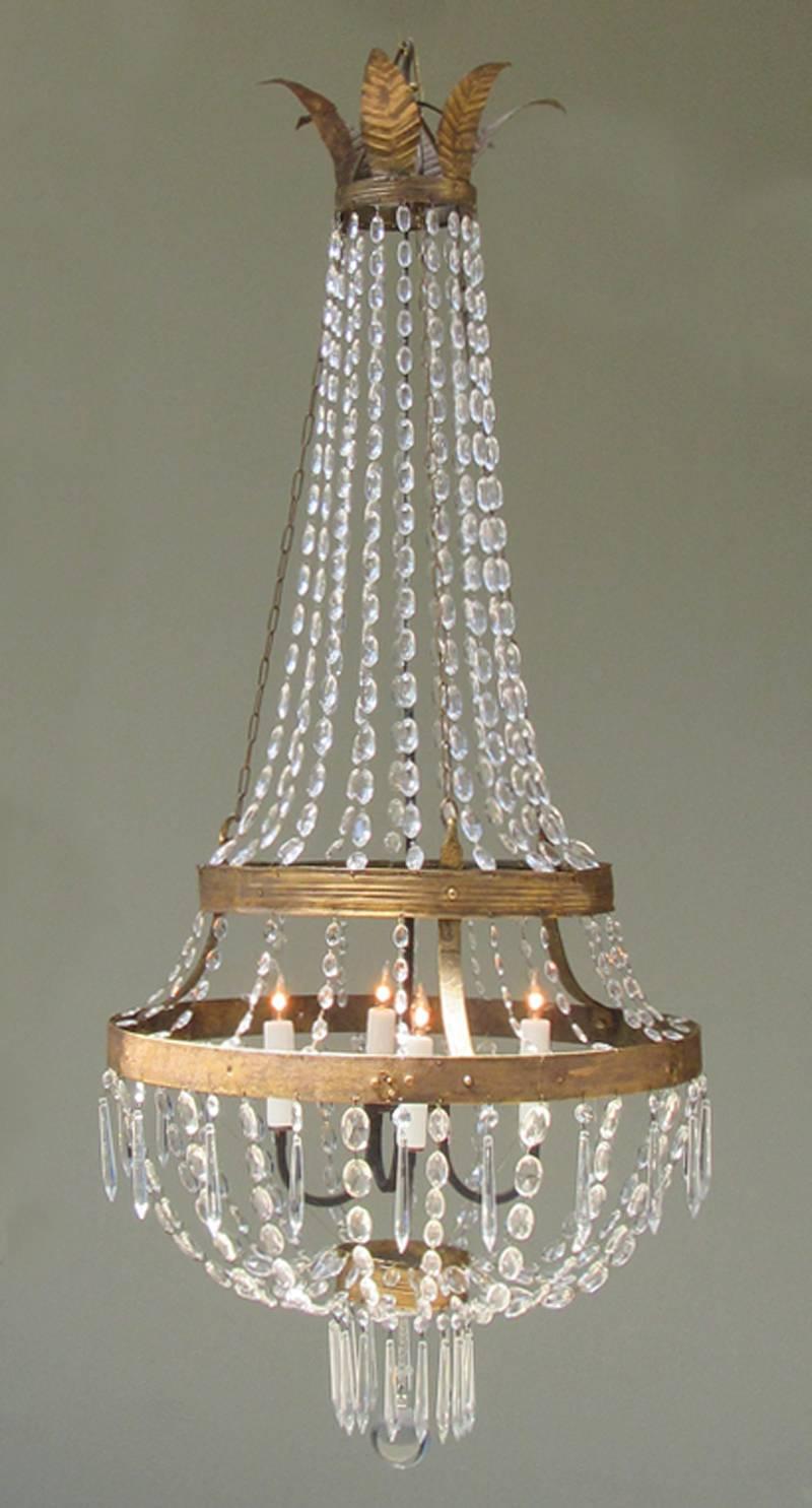 A late 18th century Italian Empire iron, tole and crystal chandelier, circa 1780, featuring gilt leaf corona and crystal basket shaped body. The chandelier was originally candle but has been rewired with a new porcelain four candle bulb pendant drop.