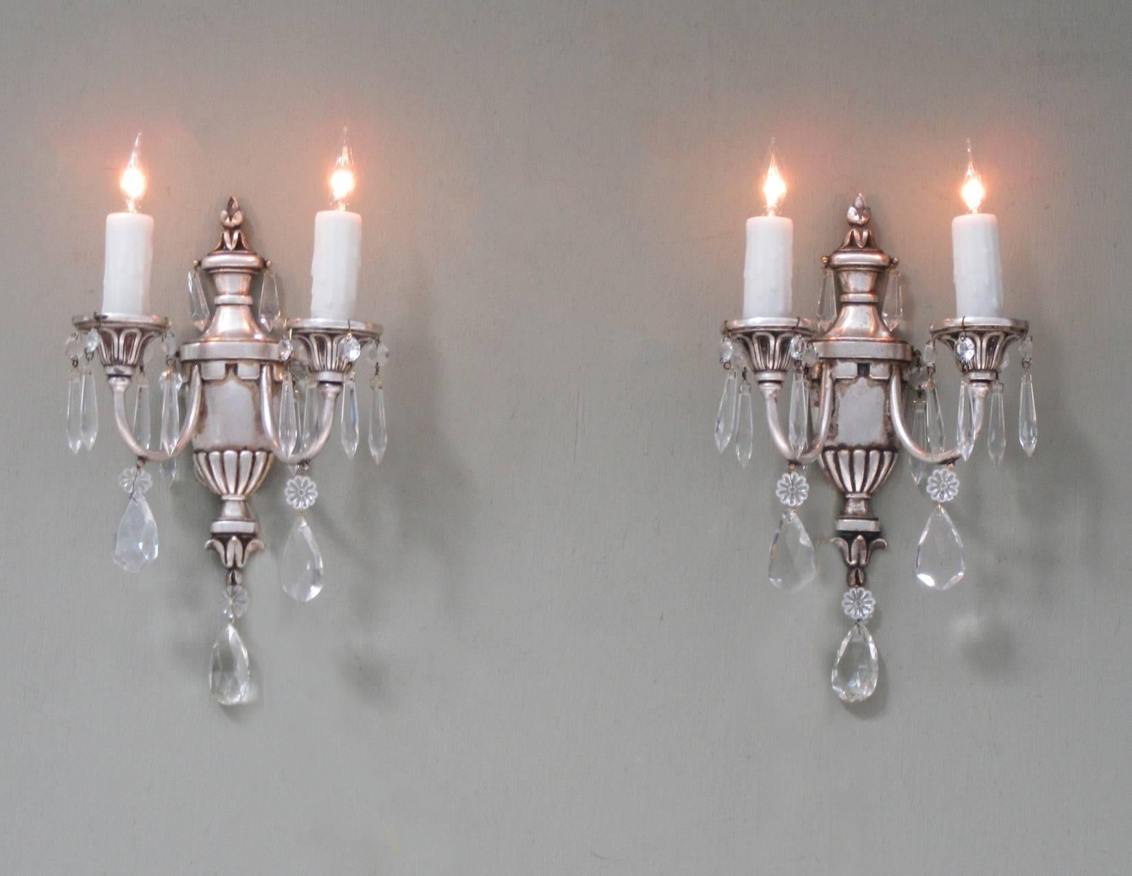 A pair of early 20th century Italian neoclassical silvered bronze and crystal sconces, featuring urn shaped bases, two candle arms and fine cut crystal pendants. The sconces have recently been cleaned and rewired with new porcelain sockets.