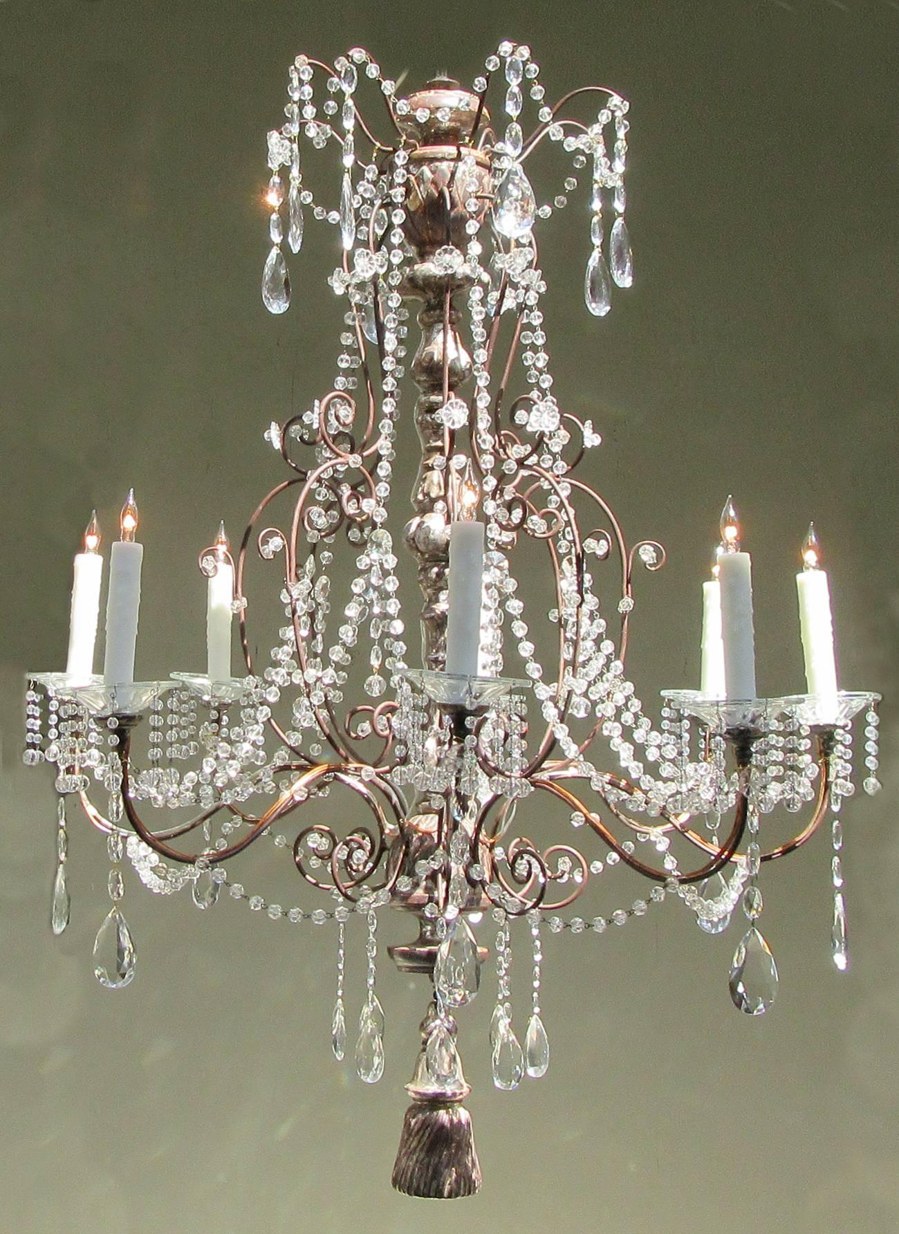 A large early 19th century Italian Baroque crystal chandelier, circa 1810, with silvered carved wood stem, eight tole candle arms with crystal beaded bobeches with large cut crystal pendants and large silvered carved wood tassel. The chandelier has