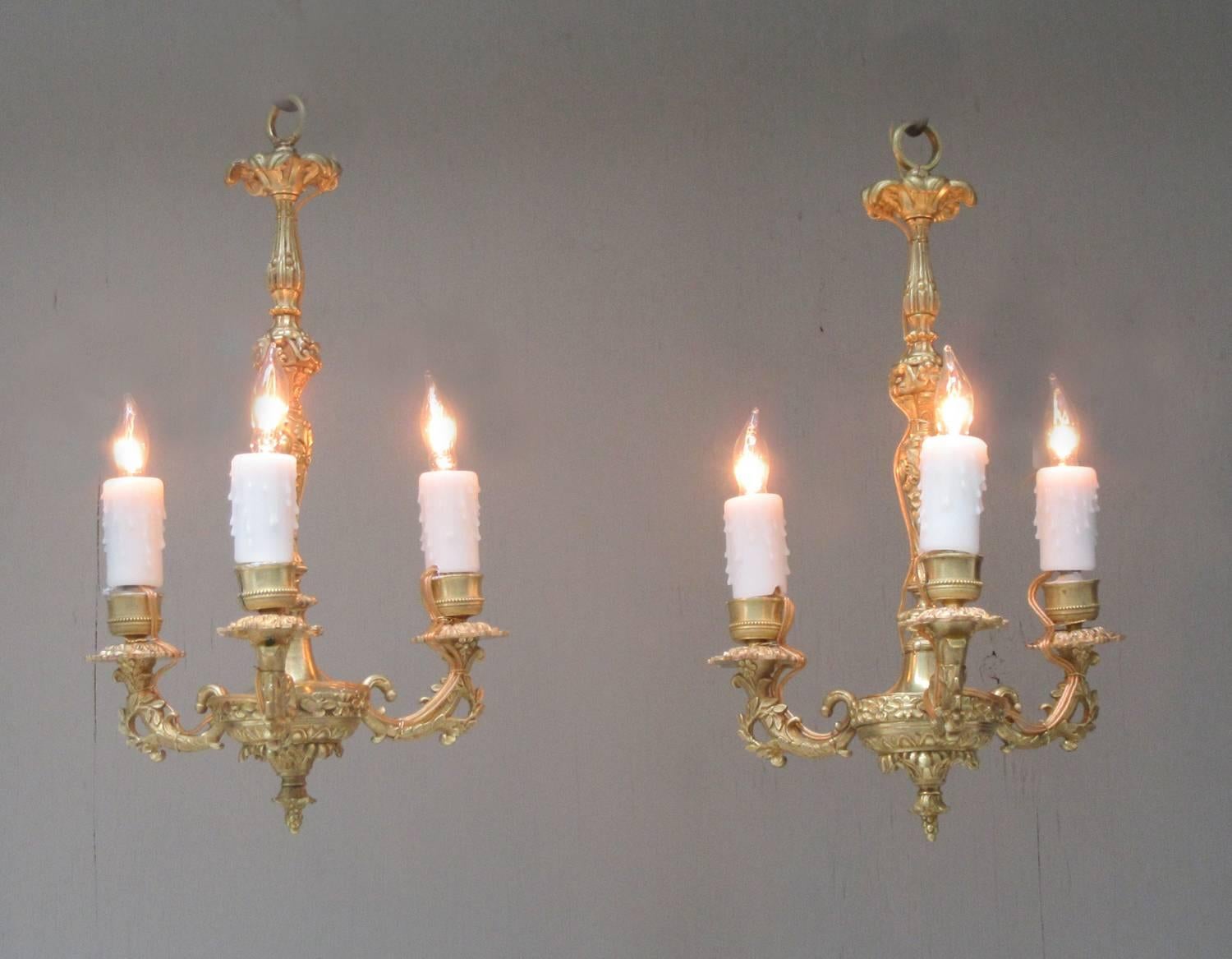 A diminutive pair of French Louis XIV bronze doré chandeliers, circa 1810, featuring finely detailed casting and three candle arms. The pair were originally candle but have recently been French wired with new porcelain sockets.