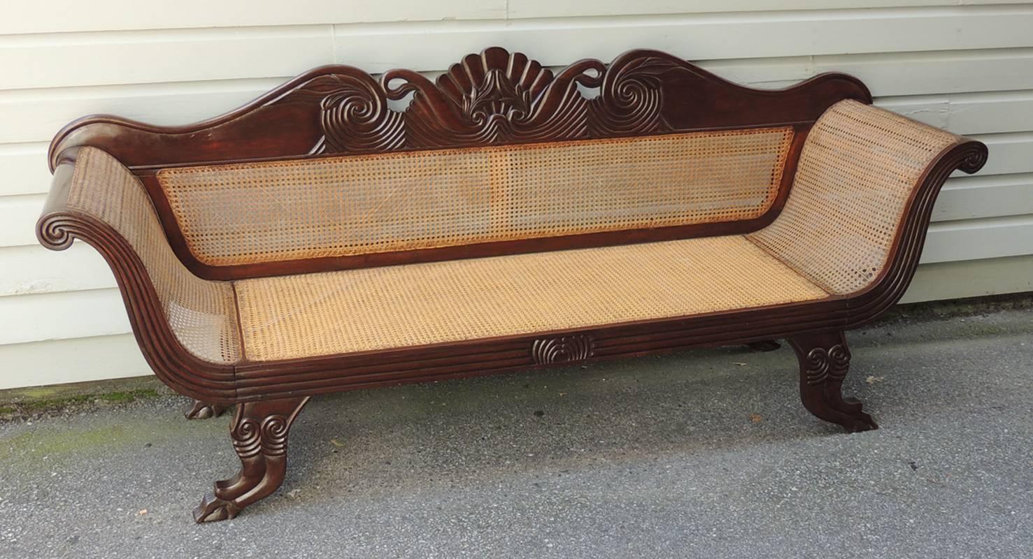 This West Indian mahogany and cane sofa was created in Jamaica during the early-19th century, circa 1820. The Caribbean sofa features a carved crest with wave motif, traditional Regency style curved arms and stylized paw feet.
 