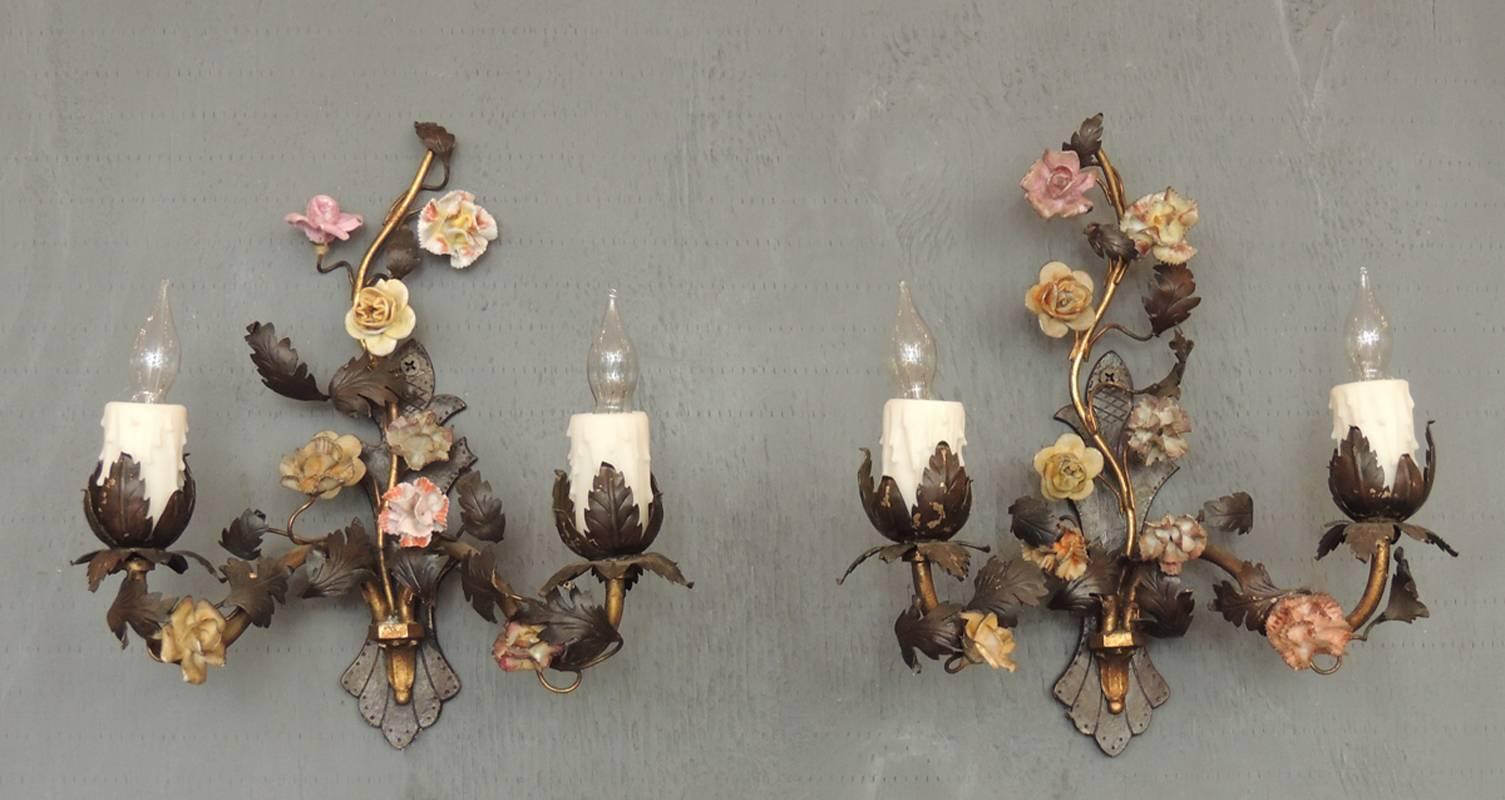 This French pair of sconces were made in the early half of the 20th century, circa 1920, and feature a bronze base with foliage and porcelain flowers.  Each sconce has two arms and eight porcelain flowers ranging in several different colors. The