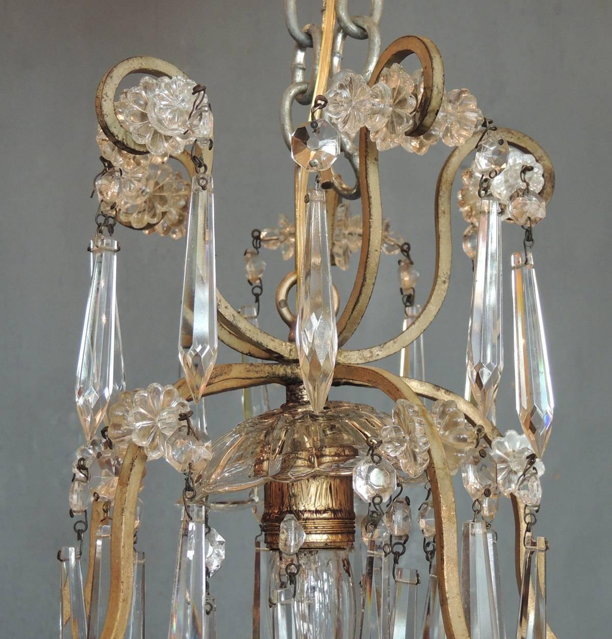 This small French Neoclassical brass and crystal chandelier lantern made in the first half of the 20th century, circa 1910. The body of the chandelier is a stylized birdcage shape decorated with crystal prisms, rosettes and drops. The fixture has