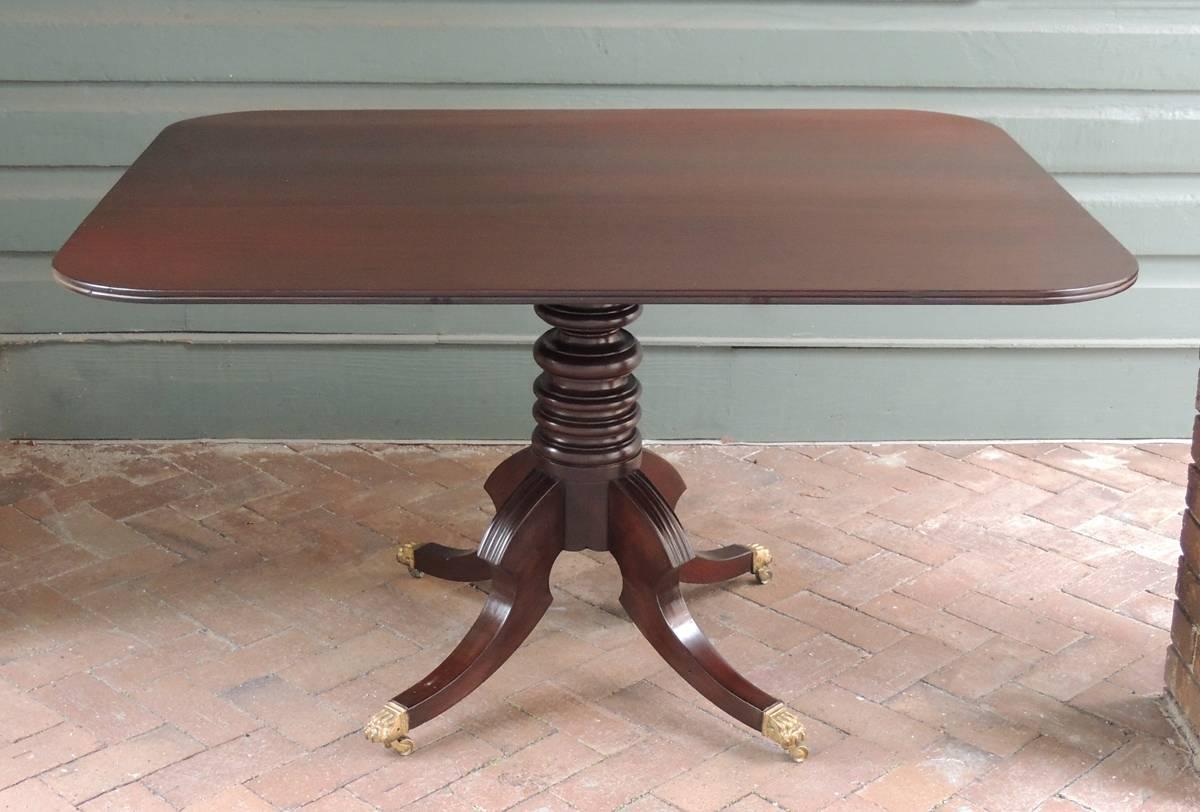 This West Indies tilt-top breakfast table was created in Jamaica in the early 19th century, circa 1800. The table is made of solid mahogany from the Caribbean and is mounted on a stacked ring pedestal base with four spur knees and brass-mounted paw
