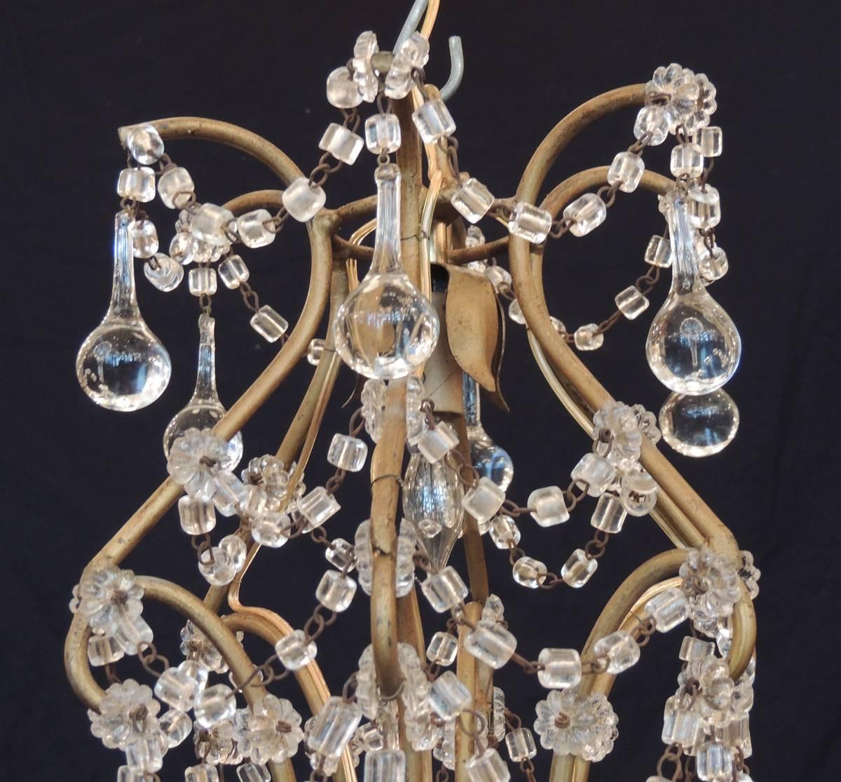 Ce lustre italien a été fabriqué à Venise au cours de la première moitié du 20e siècle, vers 1930, et présente un cadre de style cage à oiseaux avec trois bougies décorées d'une houppe en cristal et de gouttes françaises. Le luminaire est construit