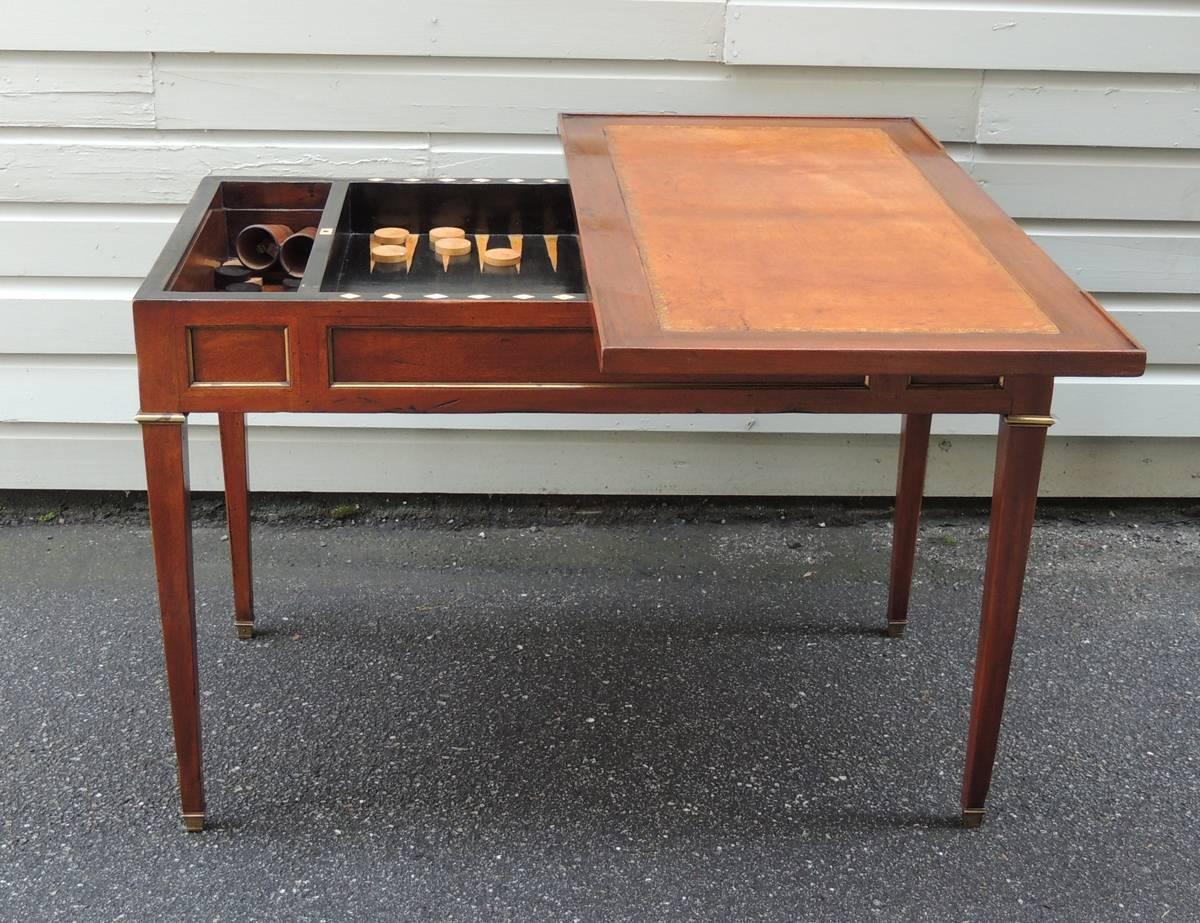 This leather top game table was made in France in the late-18th century, circa 1790. The top, when removed, reveals a backgammon board containing the original game pieces. The backgammon board is flanked by two storage compartments and sits on four