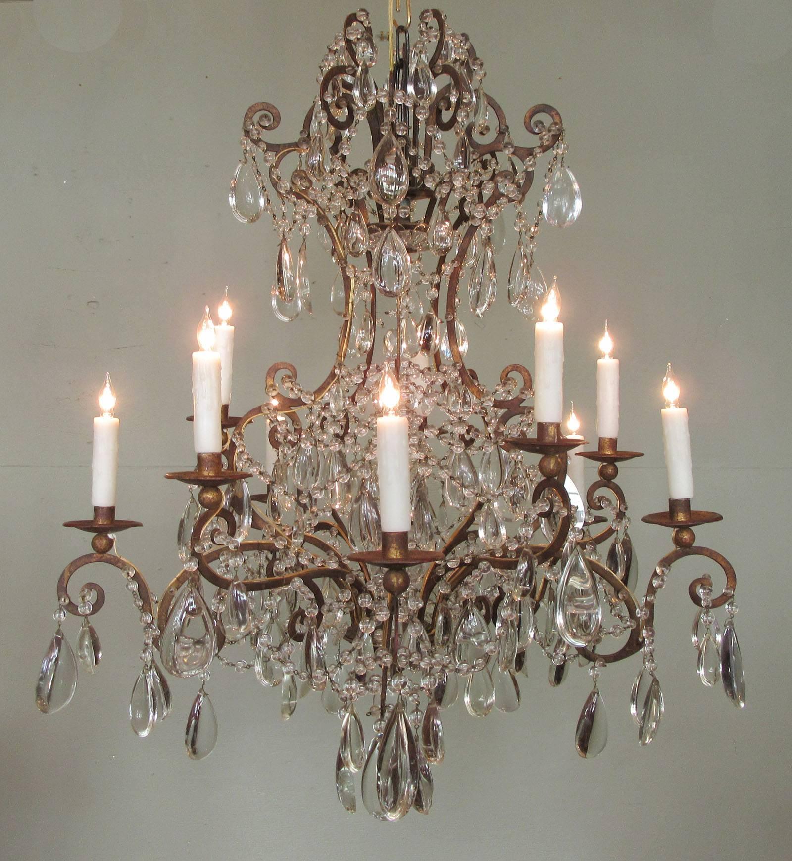 These chandeliers date to the mid-19th century, circa 1850, and were made in the Piedmont region of Italy. The fixture has ten arms and is made of tole and iron decorated with crystal prisms and swags. The chandeliers were originally candle but both