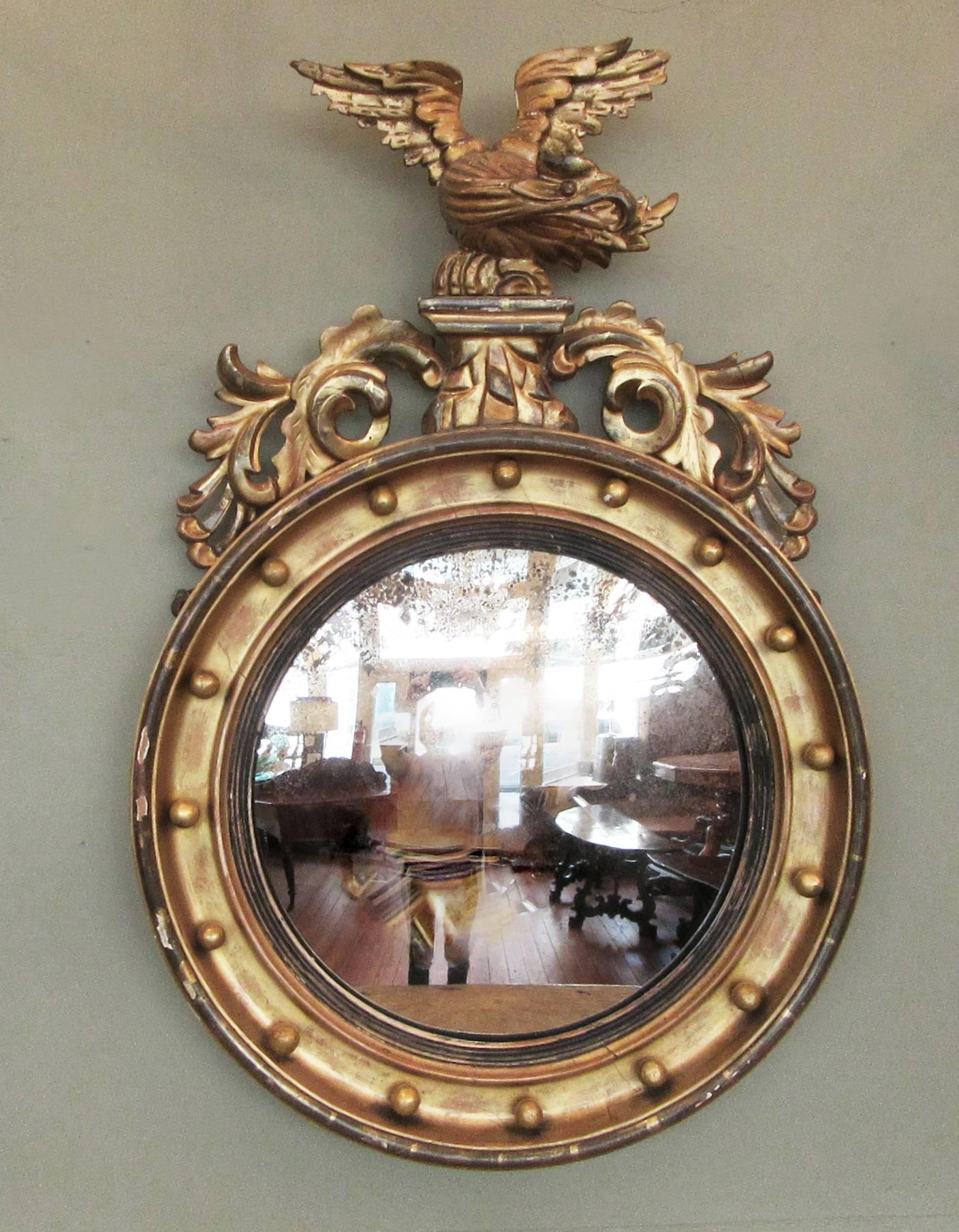 A classic English Regency convex mirror, circa 1840, made of carved giltwood and featuring a displayed eagle and acanthus leaves.