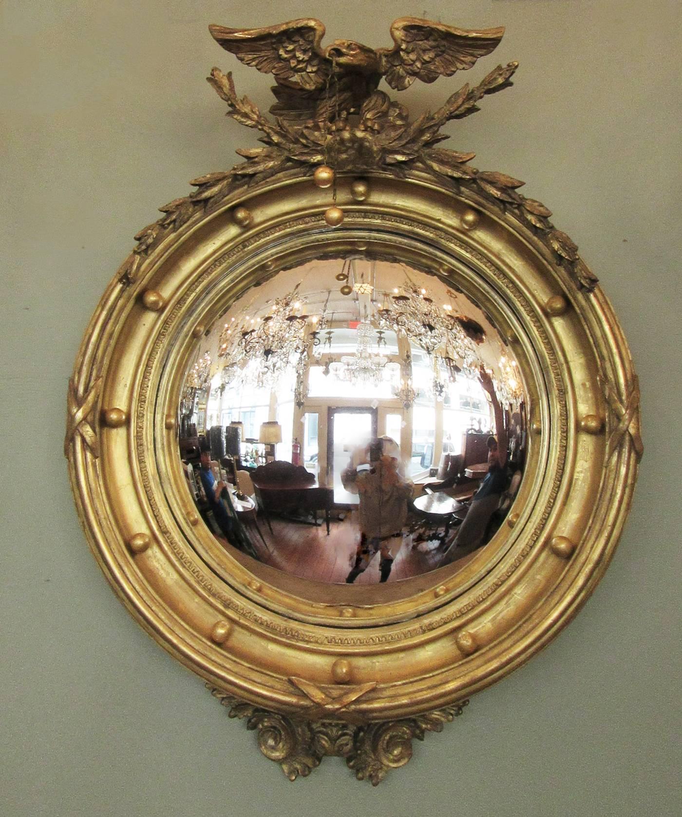 A finely gilded English Regency convex mirror, circa 1815, featuring carvings of displayed eagle with ball tassel and laurel garland.