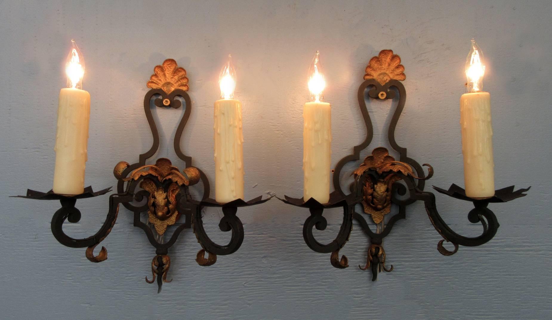 An early 20th century pair of small French Rococo iron and gilt tole sconces, circa 1910, each featuring two candle arms, shell and scrolling foliage motif.  The pair have been cleaned and recently rewired with new porcelain sockets.