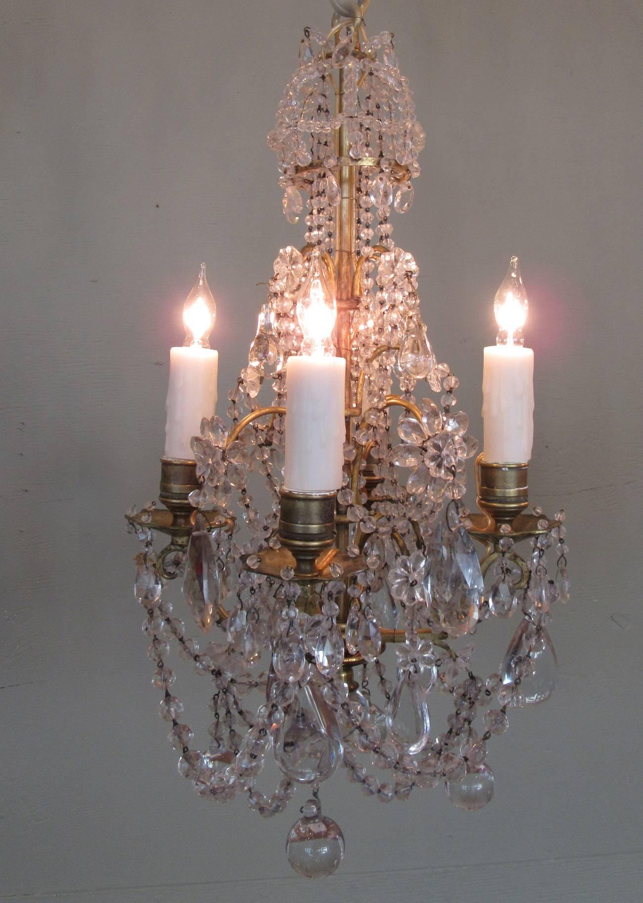 A diminutive early 19th century French Regence crystal and bronze chandelier, circa 1820, with four candle arms and adorned polished crystal pendants, beads and floral crystal accents. The chandelier has recently been cleaned and rewired with new