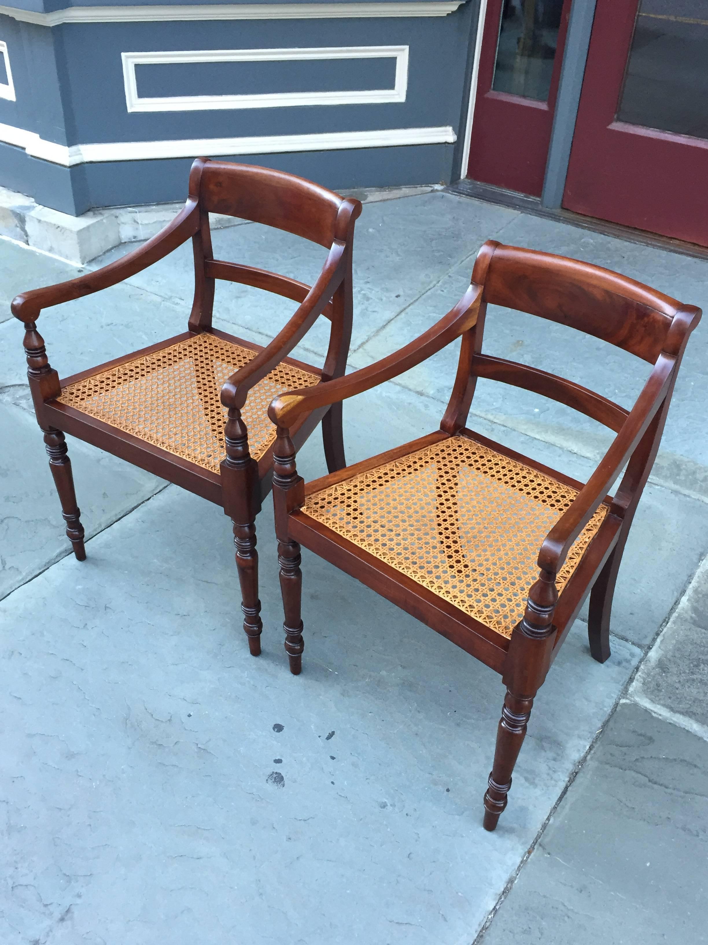 A pair of circa 1810 mahogany armchairs from Barbados, with turned legs and arm posts, shaped arms, and hand-caned seat. This pair of chairs are featured in 