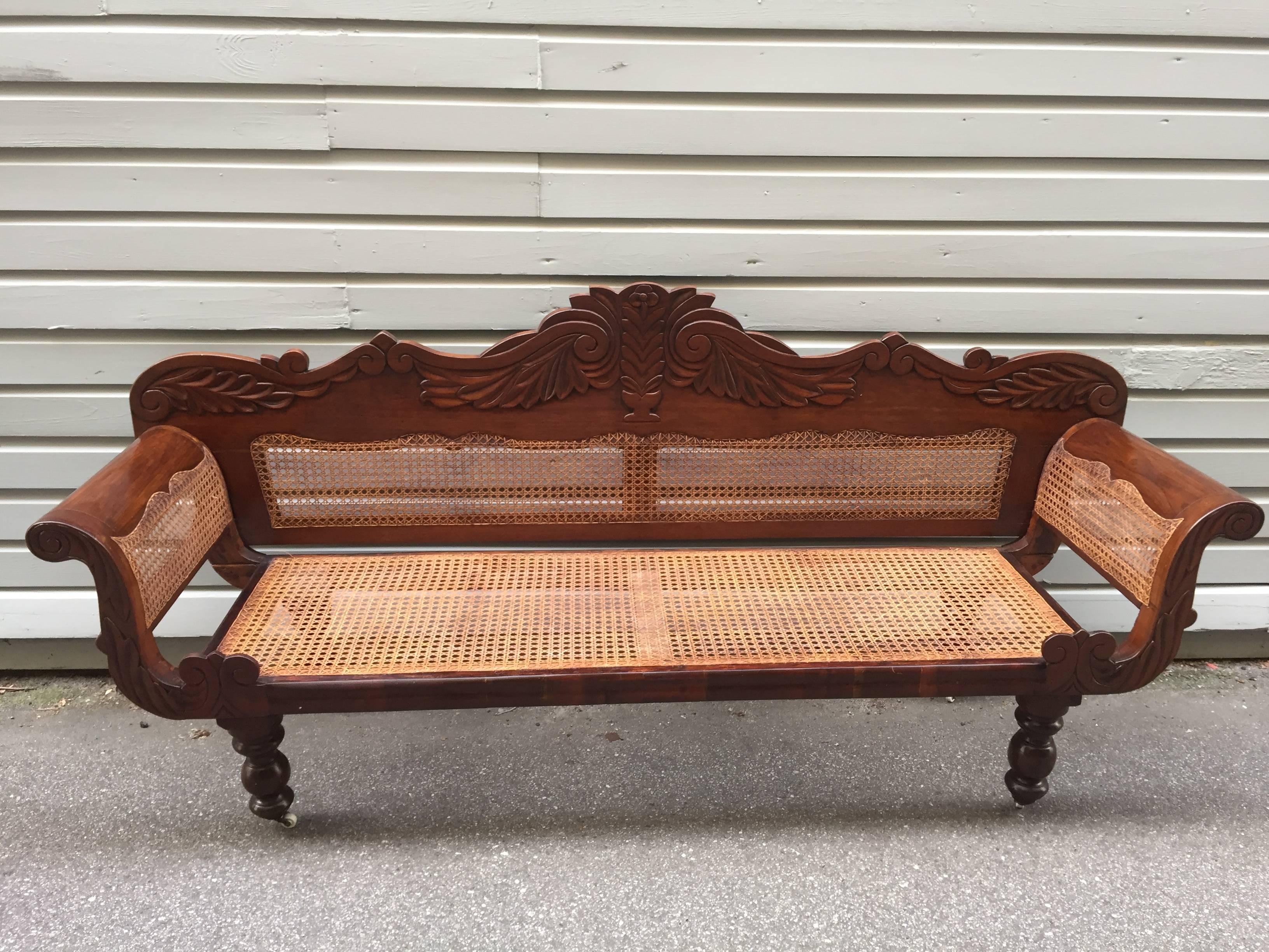 A circa 1830 cedrela settee from the West Indies, probably either Barbados or Jamaican in origin, featuring a rare and elaborate crest rail. The caned sides and back is serpentine. This piece is unusual in that the back is carved from solid cedrela.