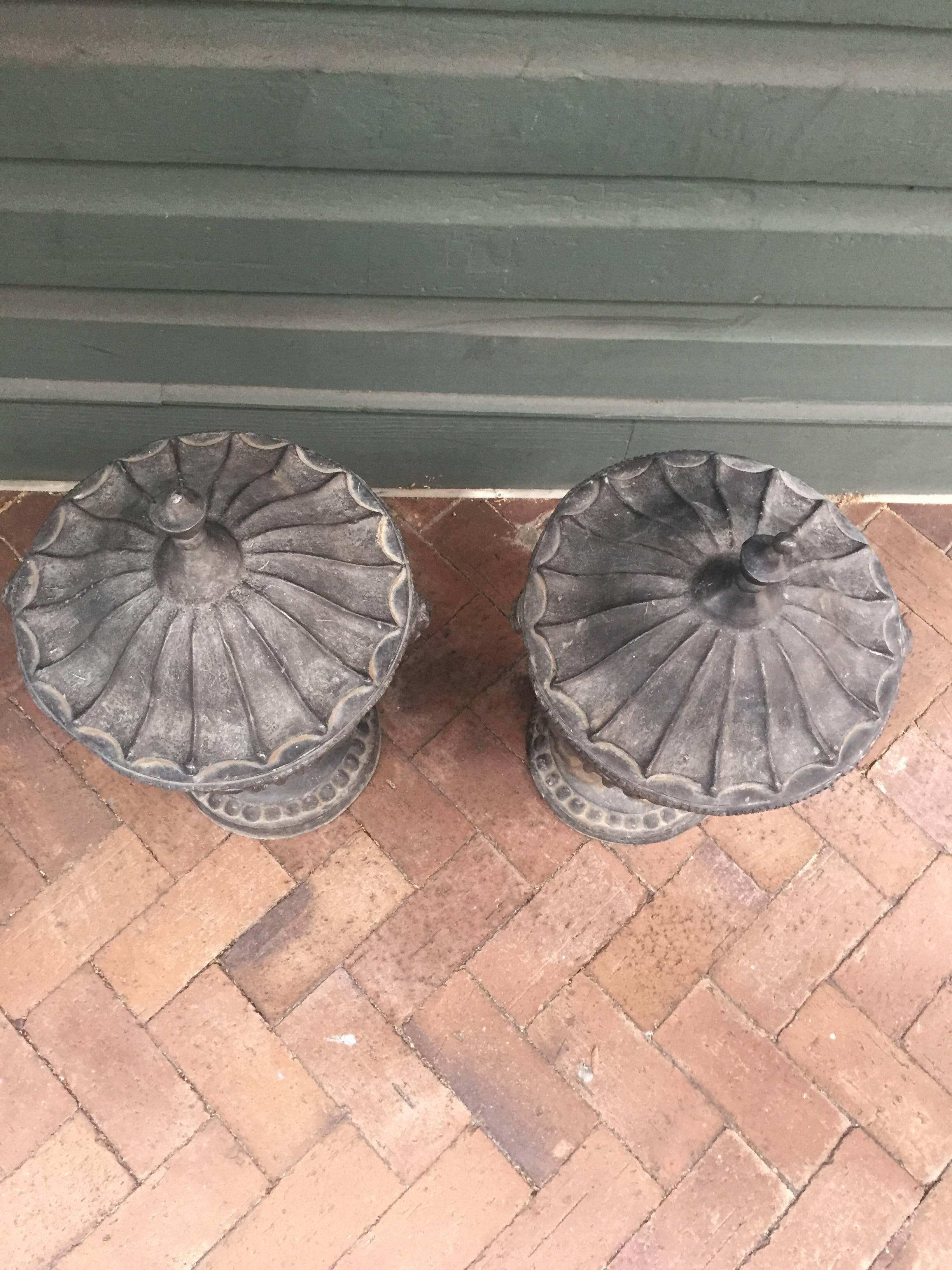 A pair of circa 1870 English urns, probably for garden us, featuring finials on top and a decorative drape motif circling the rim. These urns have had some minor repairs and one features a dent.