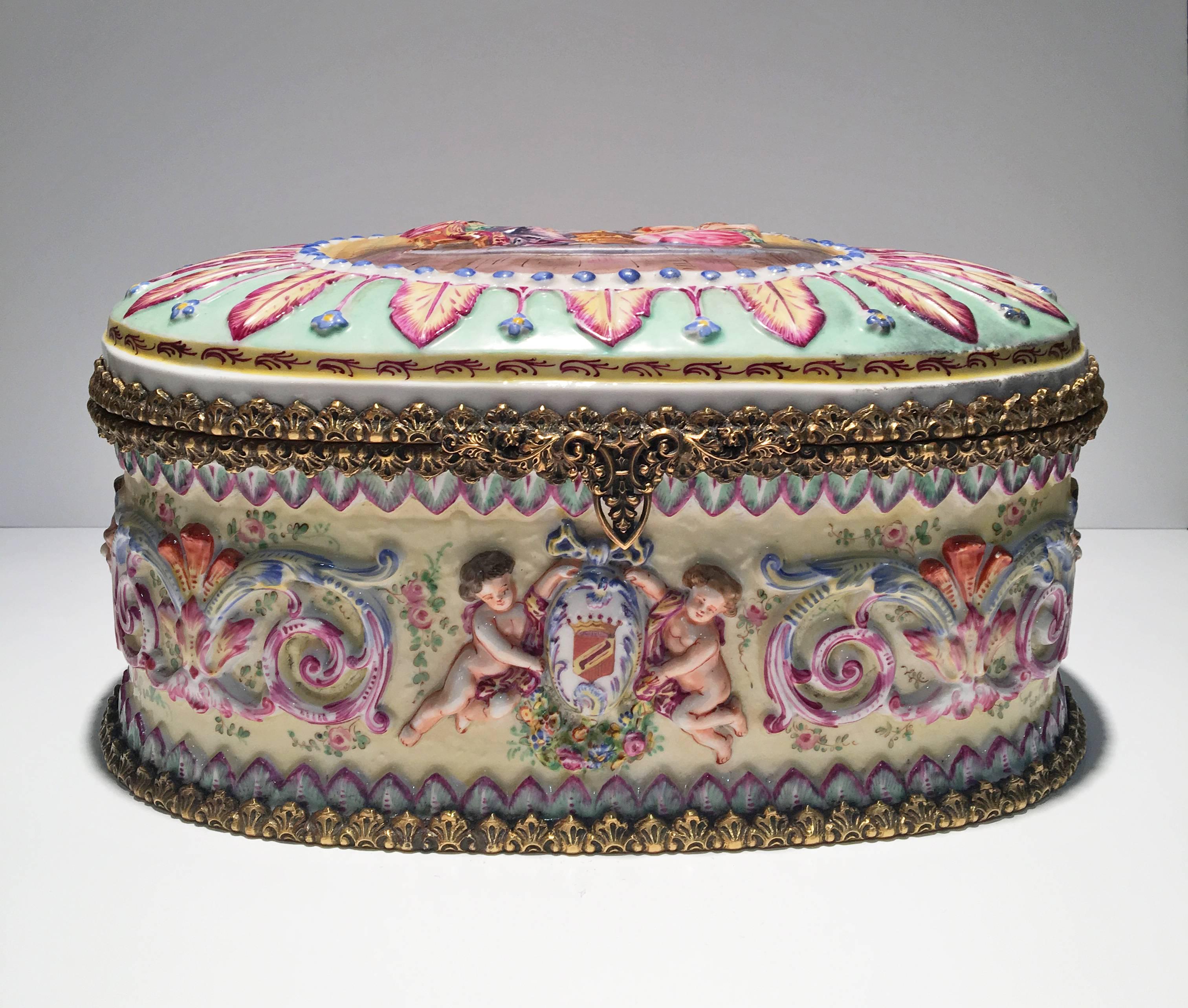 This beautiful 19th century Capo Di Monte hand painted porcelain box is decorated with colorful cherubs and the lid has scene of three women sitting around a fireplace. Distinctive 