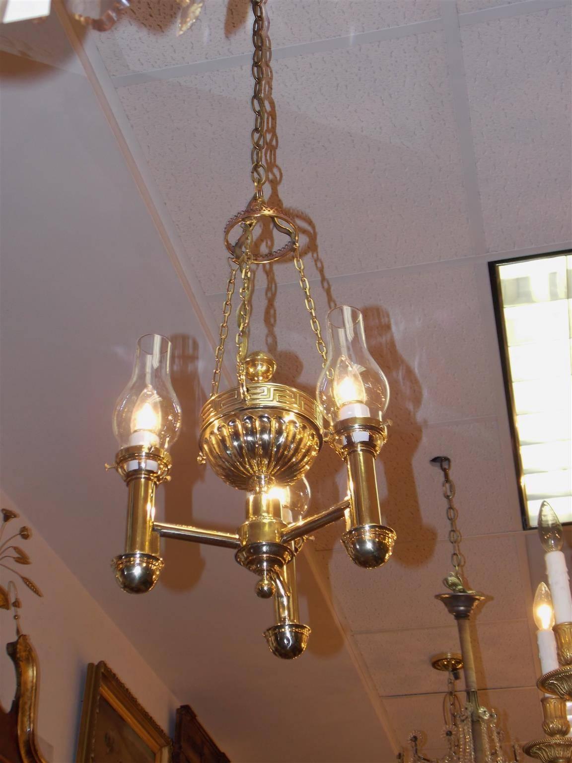 American brass three-arm argand chandelier with ribbed centered urn, Greek key motif, bulbous glass chimneys, original canopy and terminating with a ball finial. Originally oil and has been electrified. Early 19th century.