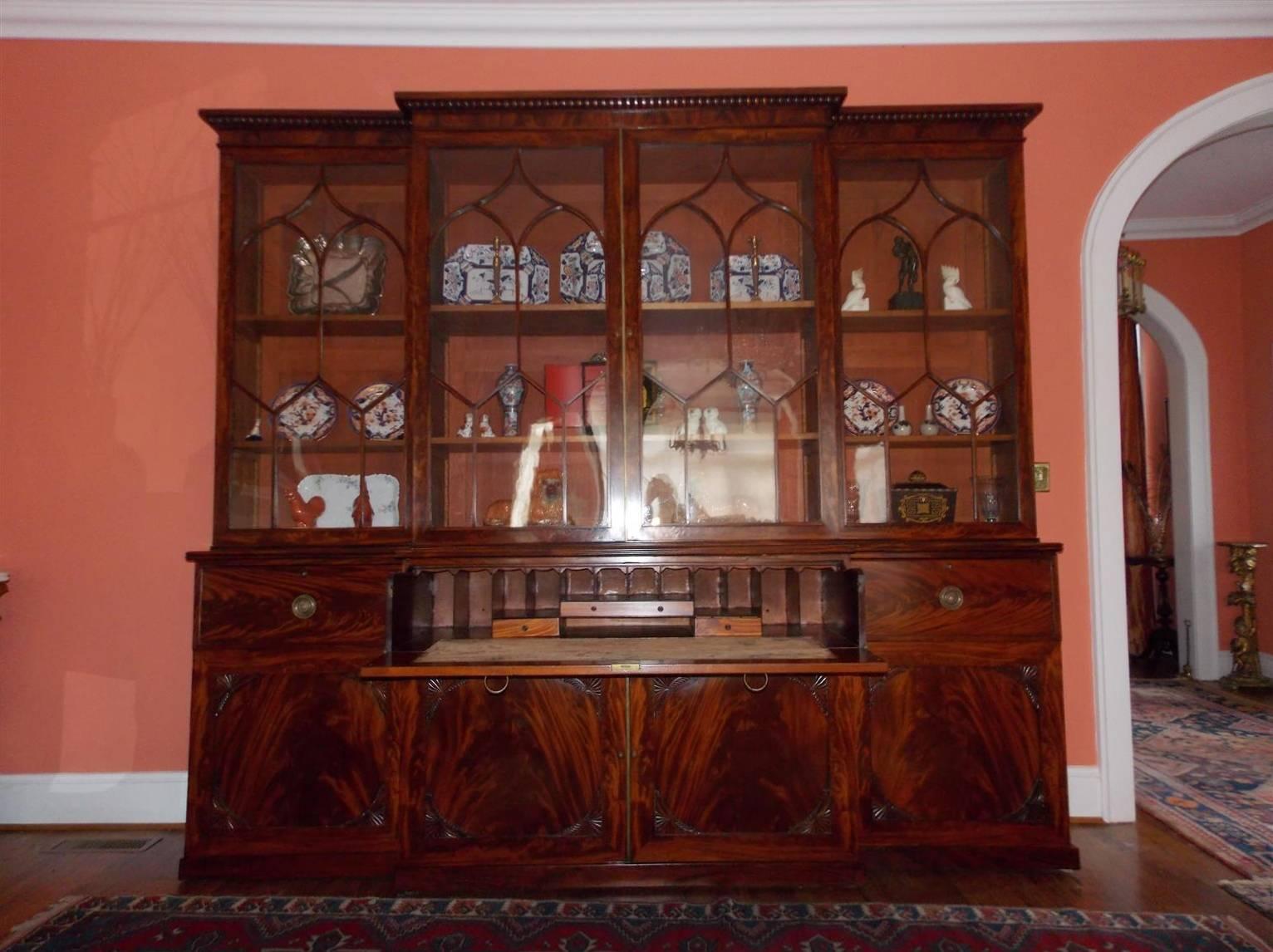 English Chippendale mahogany breakfront with carved molded cornice, four upper case glass doors with arched oval mullions, adjustable interior shelving, lower case concealing a sliding fall front desk, flanking drawers with original brasses and